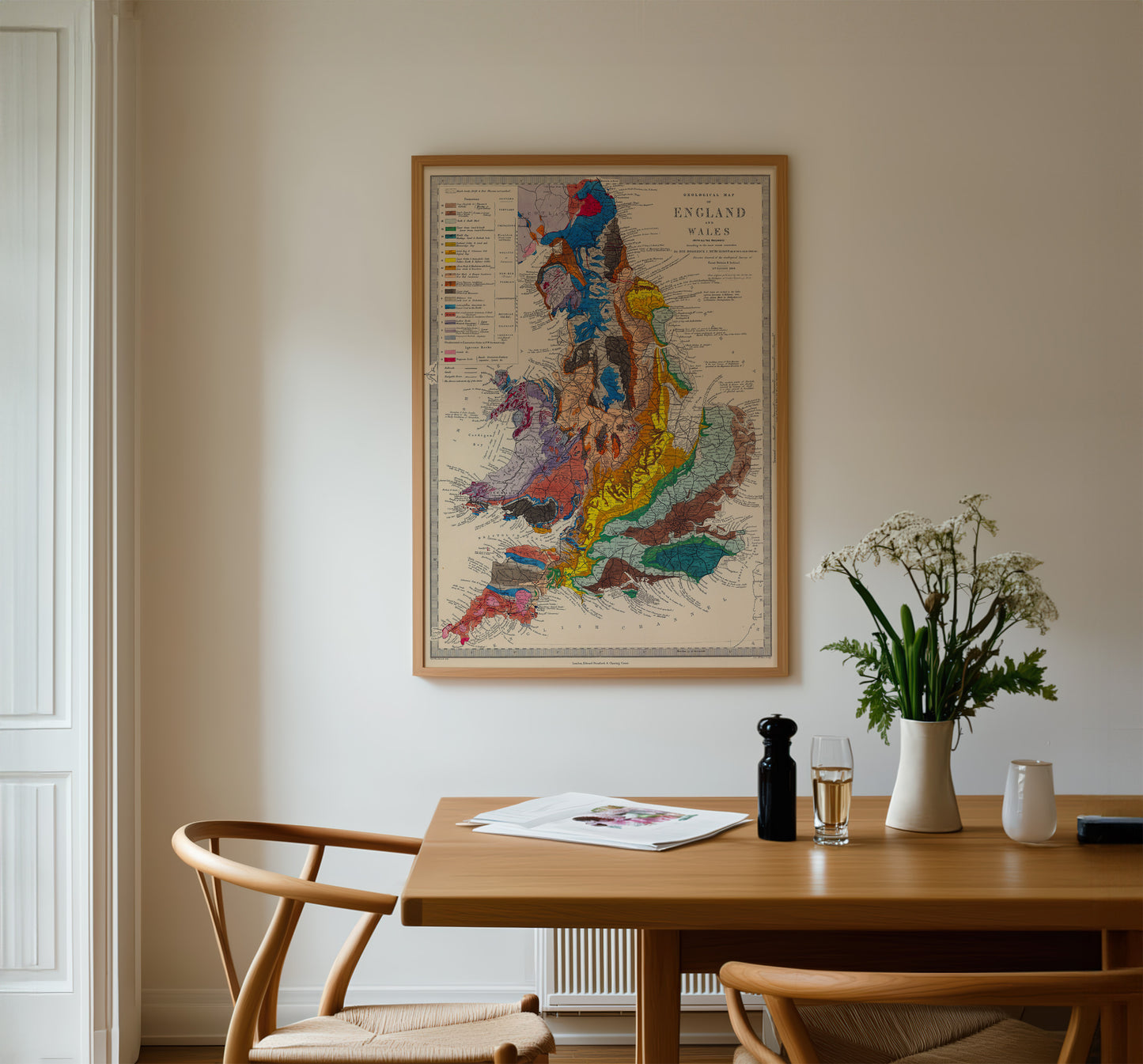 a wooden dining table with a vase of flowers, a newspaper, and a bottle of wine. Above the table, there is a framed map of England.