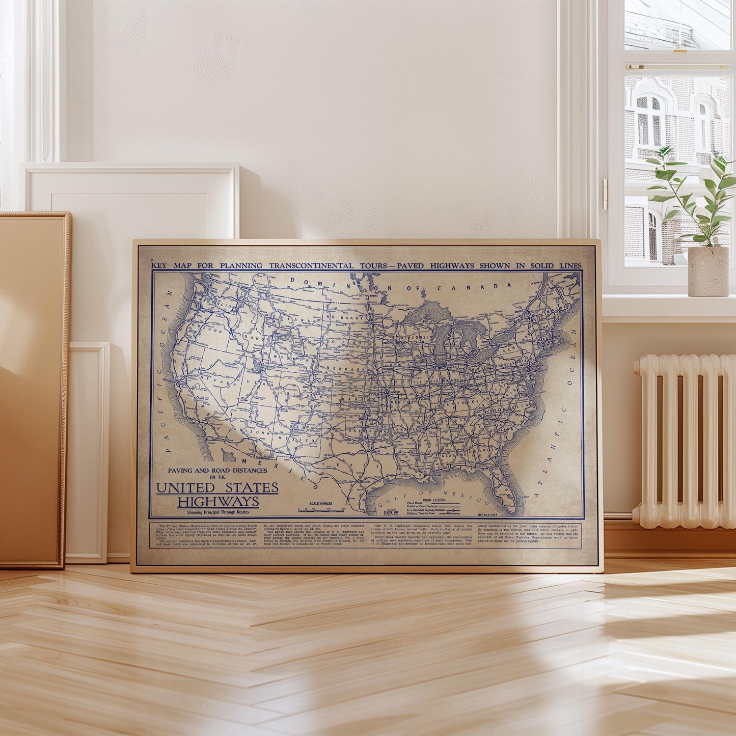 A framed map of the United States highways is displayed on a wooden floor in a room with a window and a radiator.