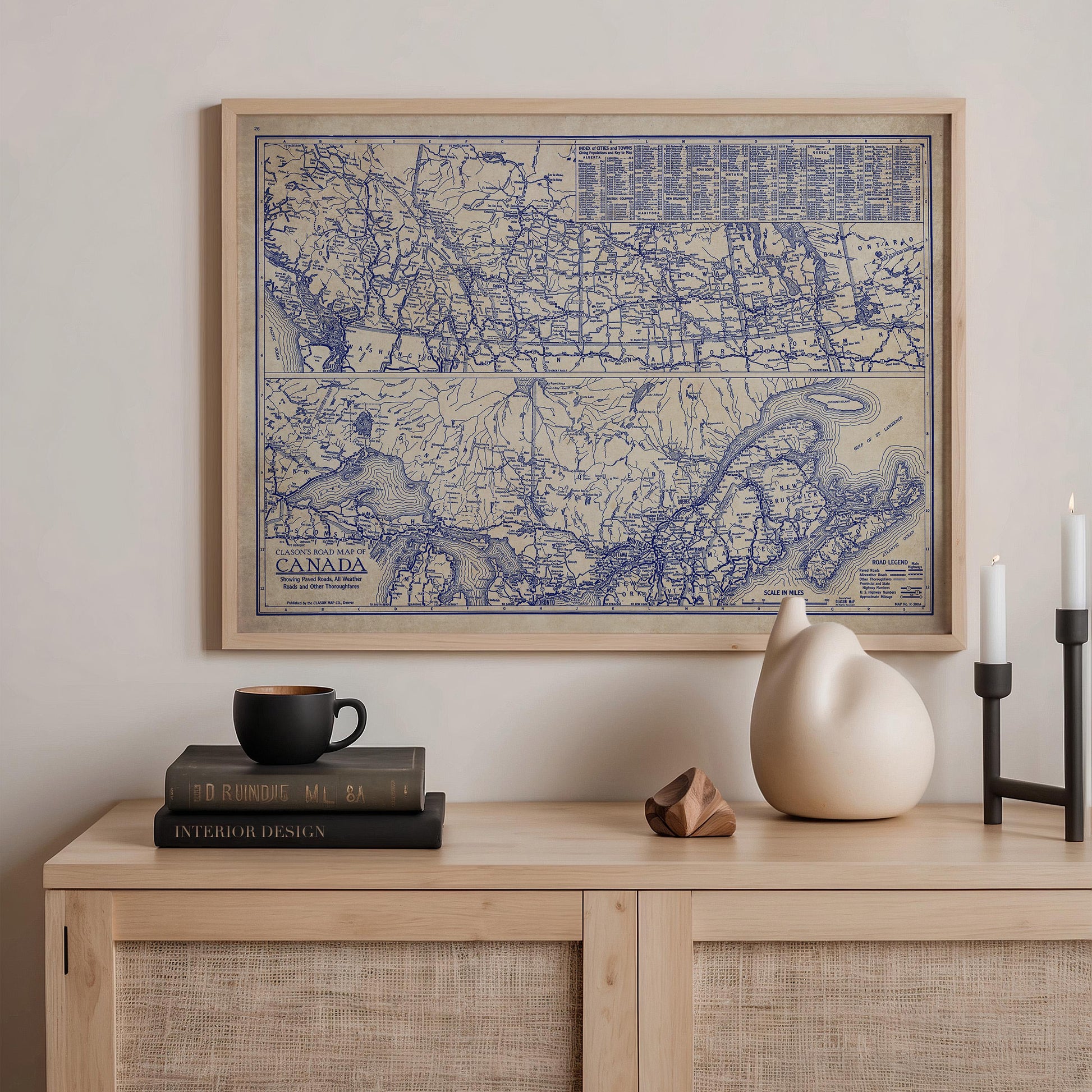 a wooden cabinet with a framed map of Canada hanging on the wall above it. On the cabinet, there are a stack of books, a ceramic cat figurine, and a small ceramic vase.