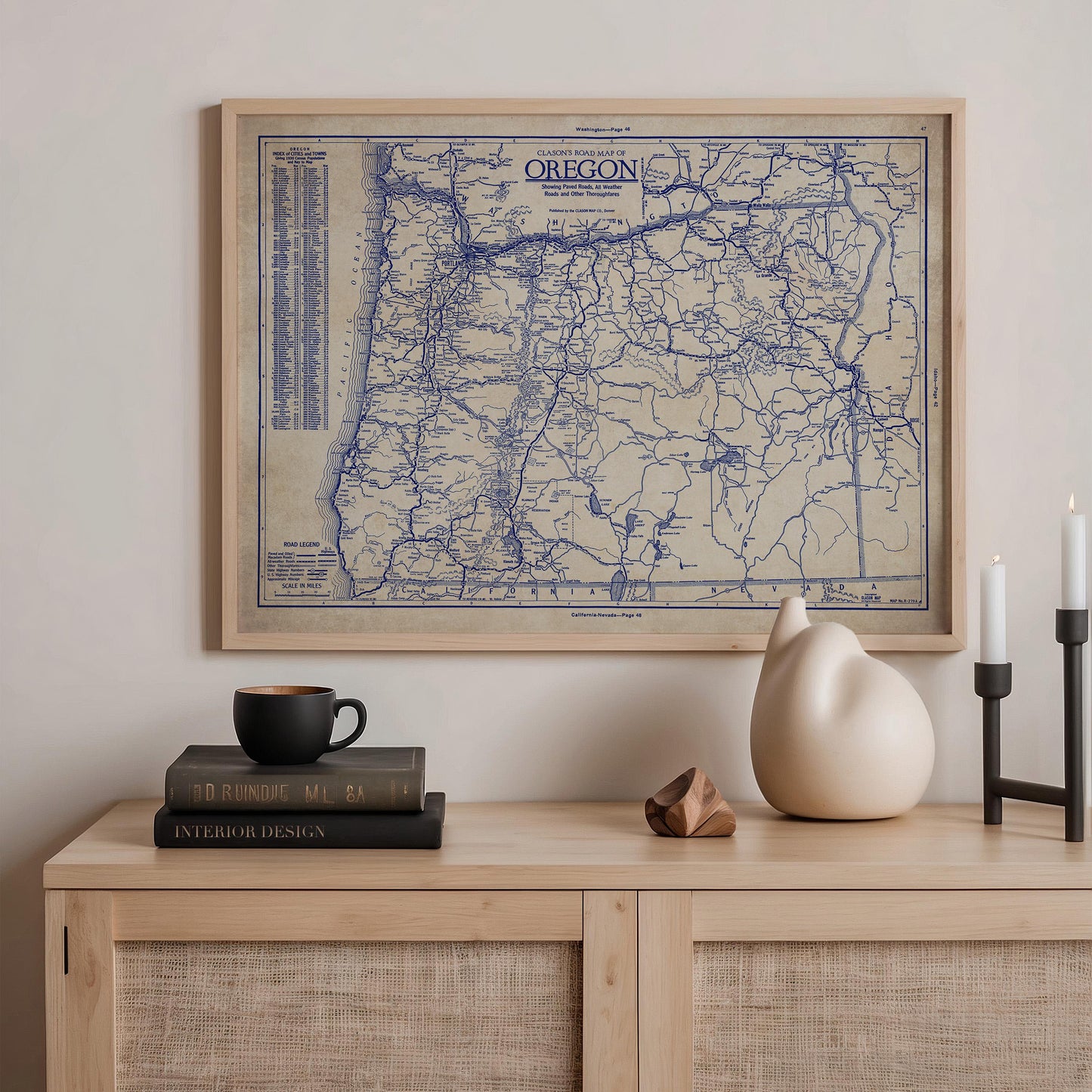 a framed map of Oregon hanging on a wall above a wooden shelf with various items on it, including a stack of books, a ceramic vase, and a small sculpture.
