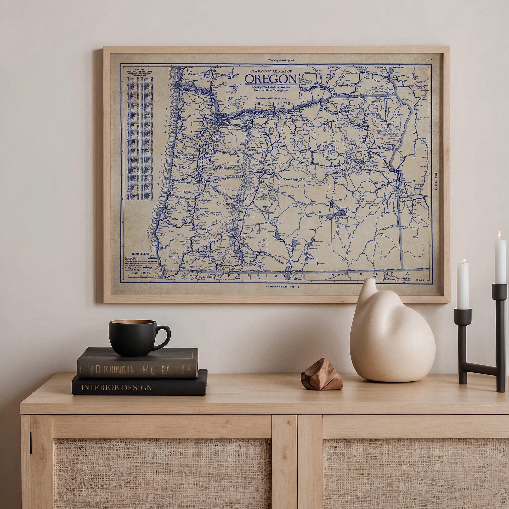 a framed map of Oregon hanging on a wall above a wooden shelf with various items on it, including a stack of books, a ceramic vase, and a small sculpture.
