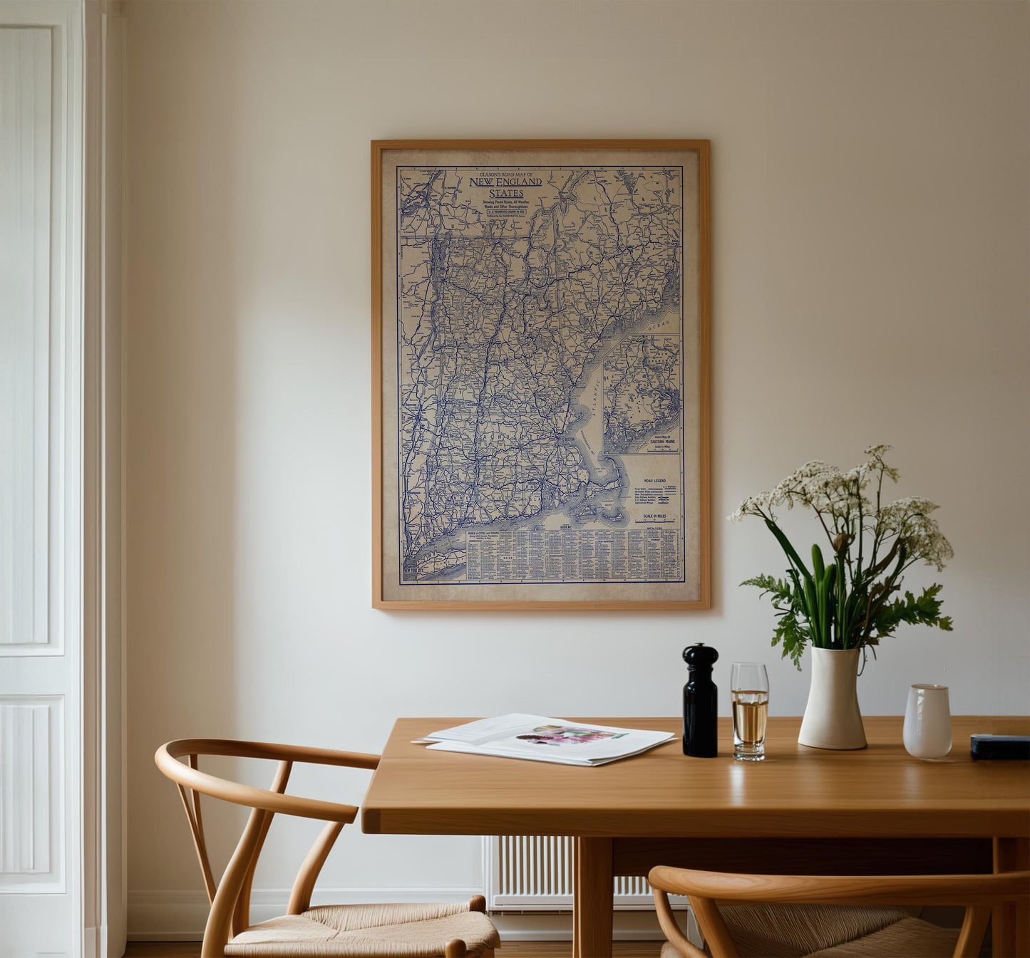 a wooden dining table with a vase of white flowers, a newspaper, and a glass of wine. Above the table, there is a framed map of the United States hanging on the wall.