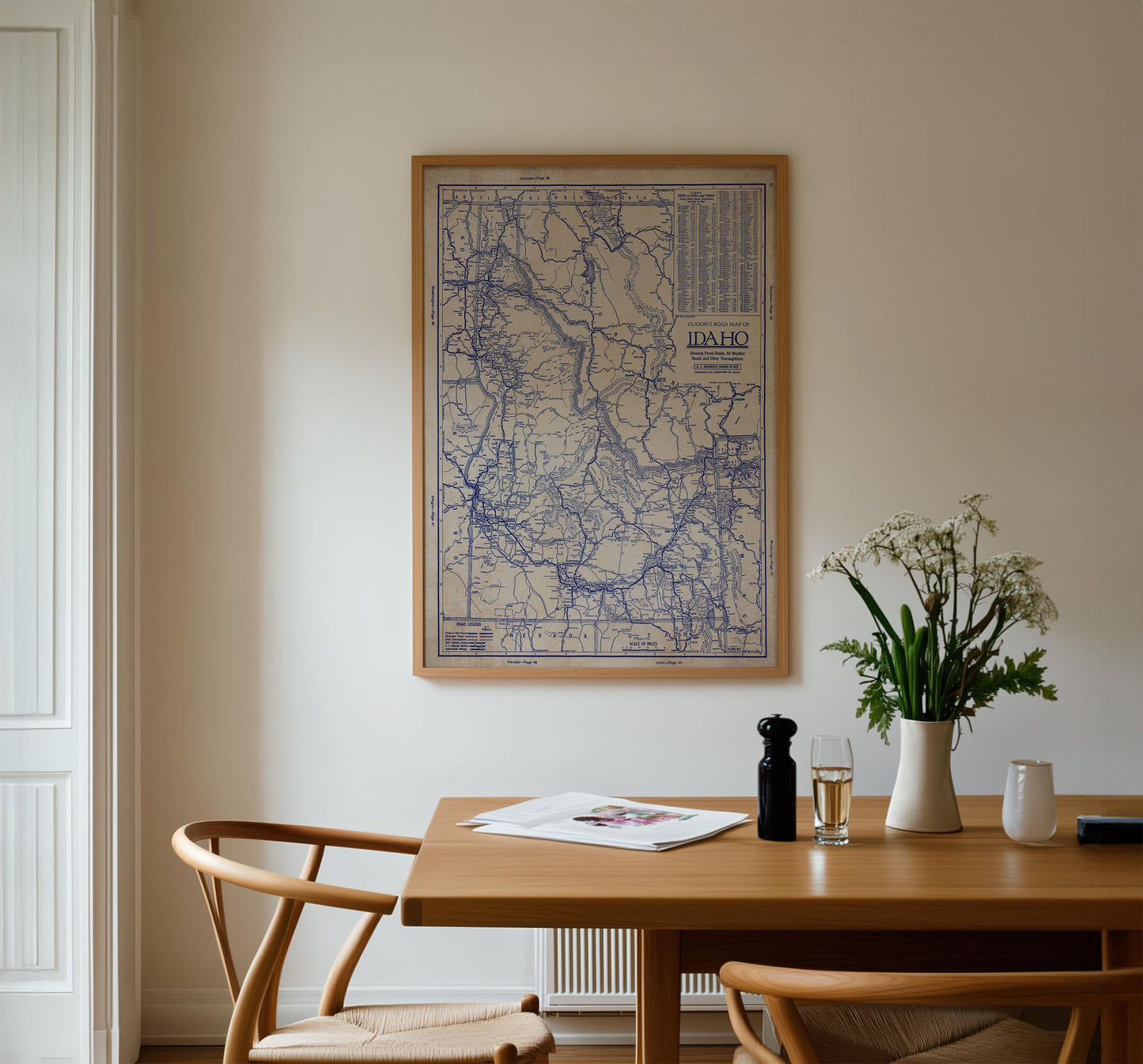 a wooden dining table with a vase of white flowers, a newspaper, and a glass of wine. Above the table, there is a framed map of the United States hanging on the wall.