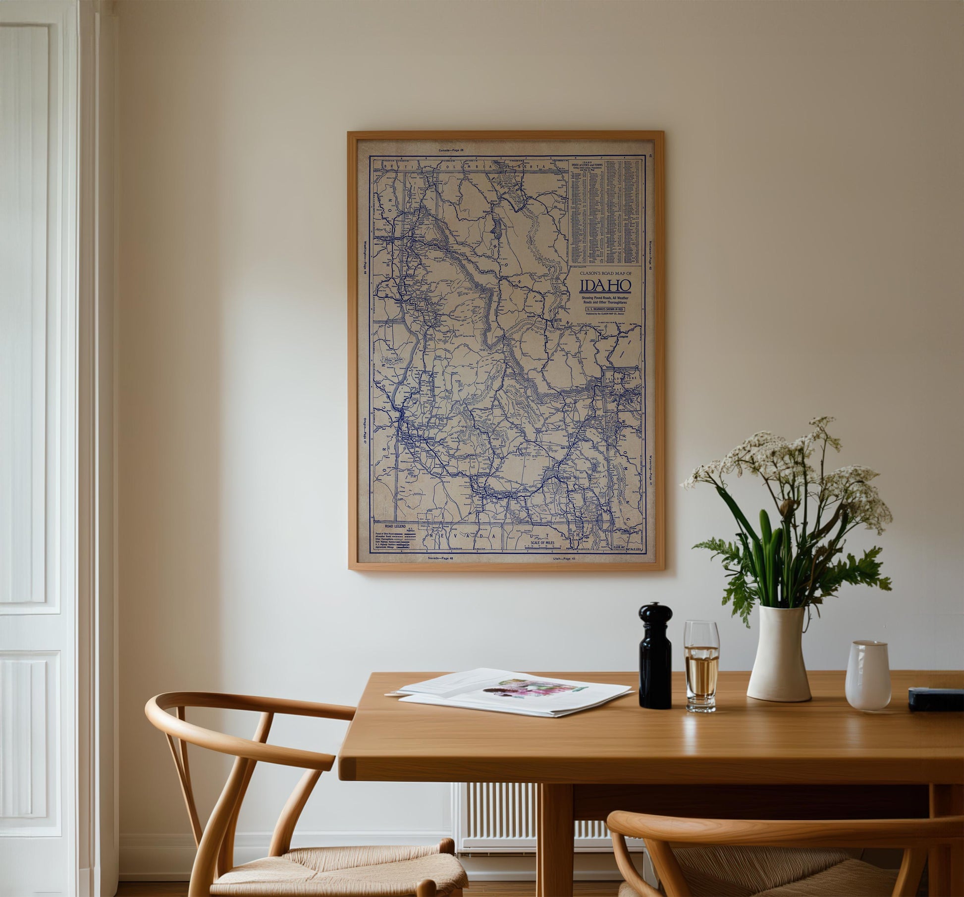 a wooden dining table with a vase of white flowers, a newspaper, and a glass of wine. Above the table, there is a framed map of the United States hanging on the wall.