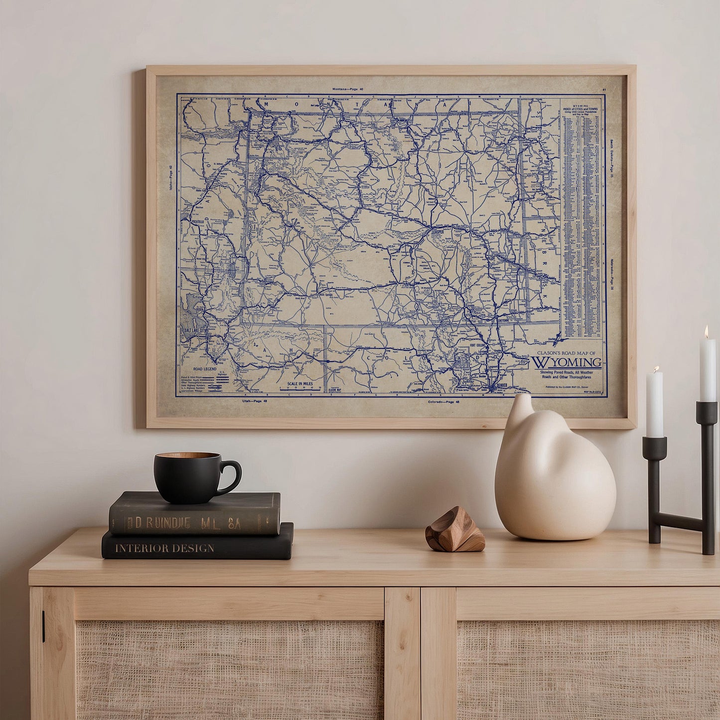 a wooden cabinet with a framed map of Wisconsin hanging on the wall above it. On the cabinet, there is a stack of books, a ceramic vase, and a small sculpture.