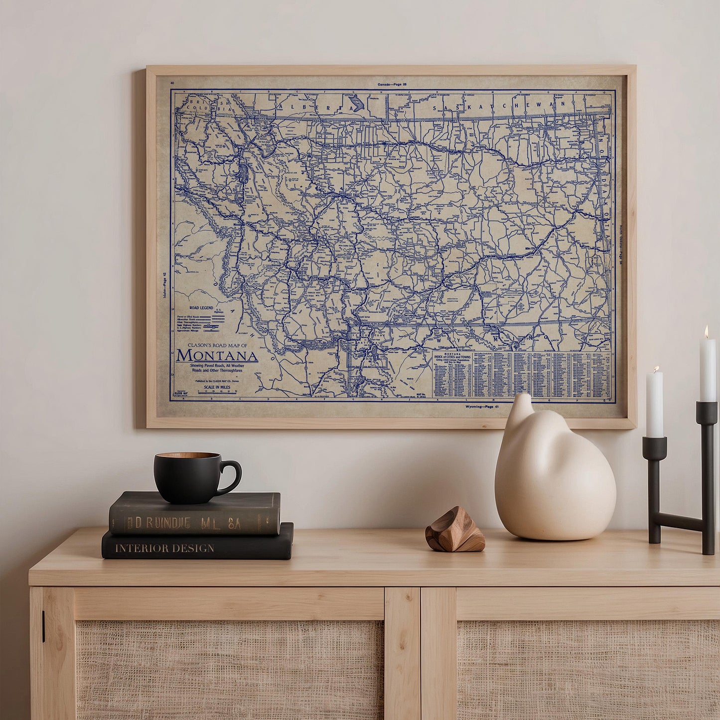 a framed map of Montana, a stack of books, a ceramic cat figurine, and a small wooden sculpture on a wooden shelf.
