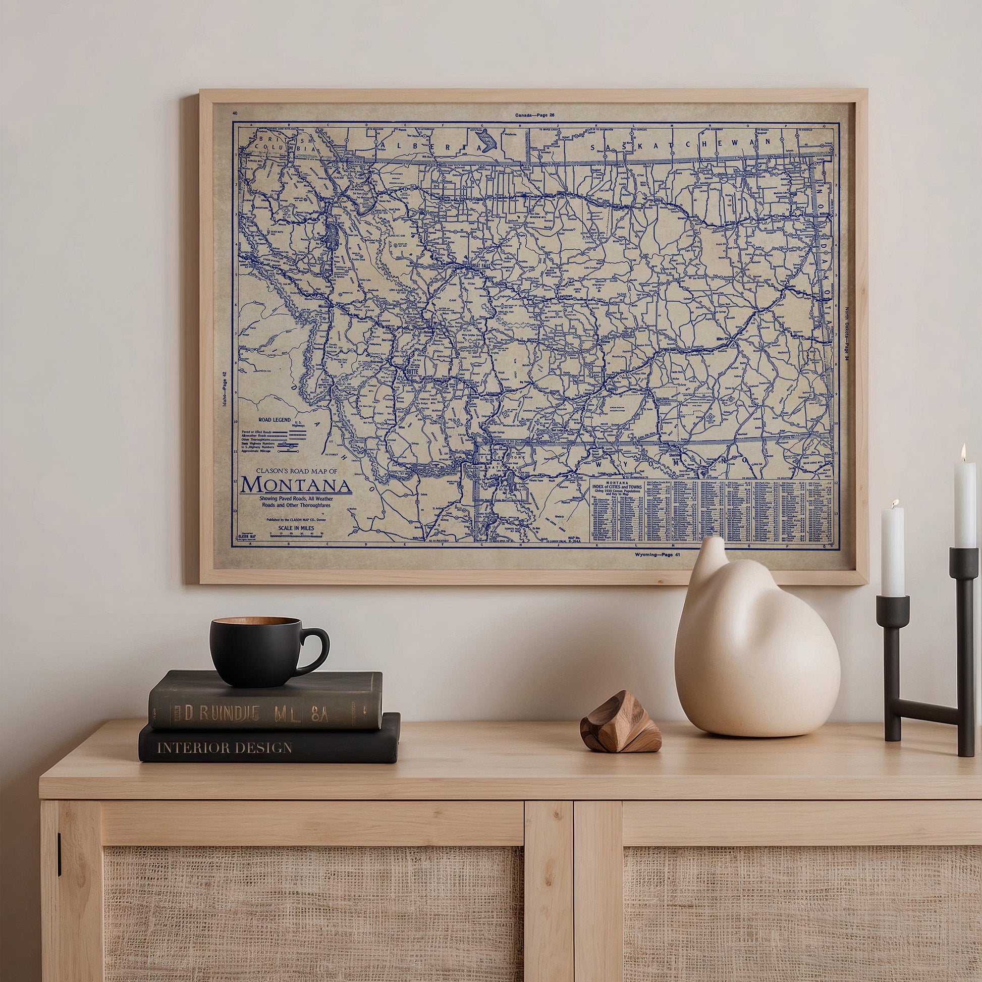 a framed map of Montana, a stack of books, a ceramic cat figurine, and a small wooden sculpture on a wooden shelf.