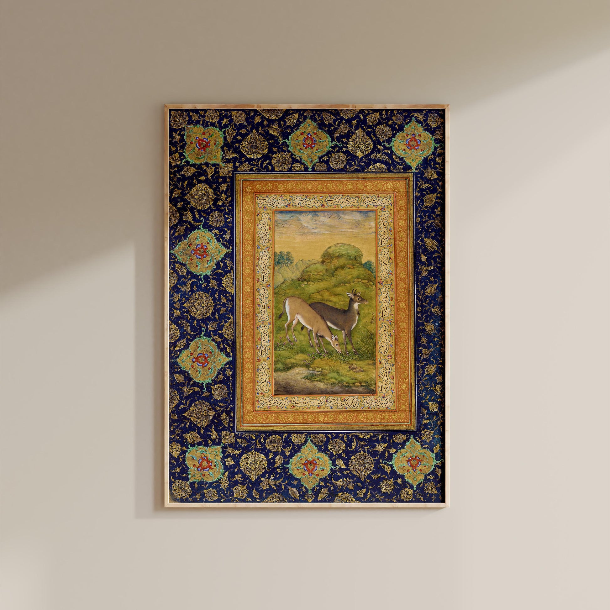 a framed painting of a deer in a grassy field, with a decorative border and floral patterns surrounding the artwork.