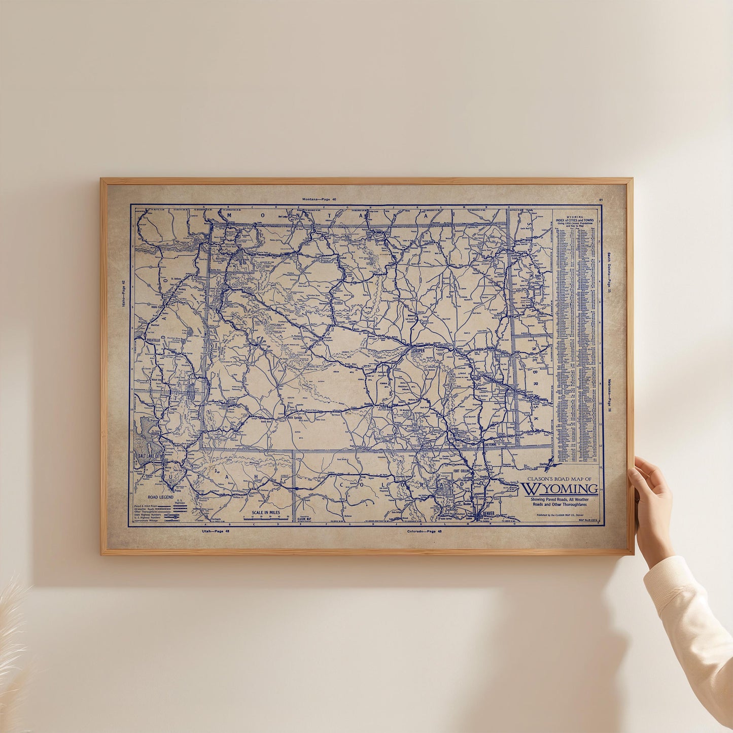 A framed map of Wyoming is being held up against a white wall.