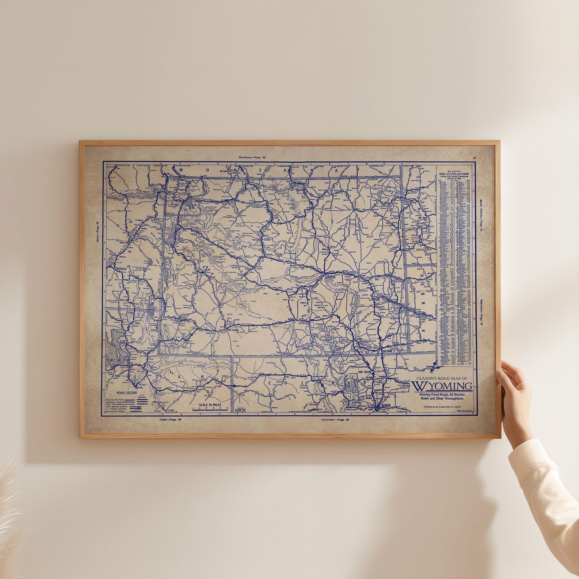 A framed map of Wyoming is being held up against a white wall.