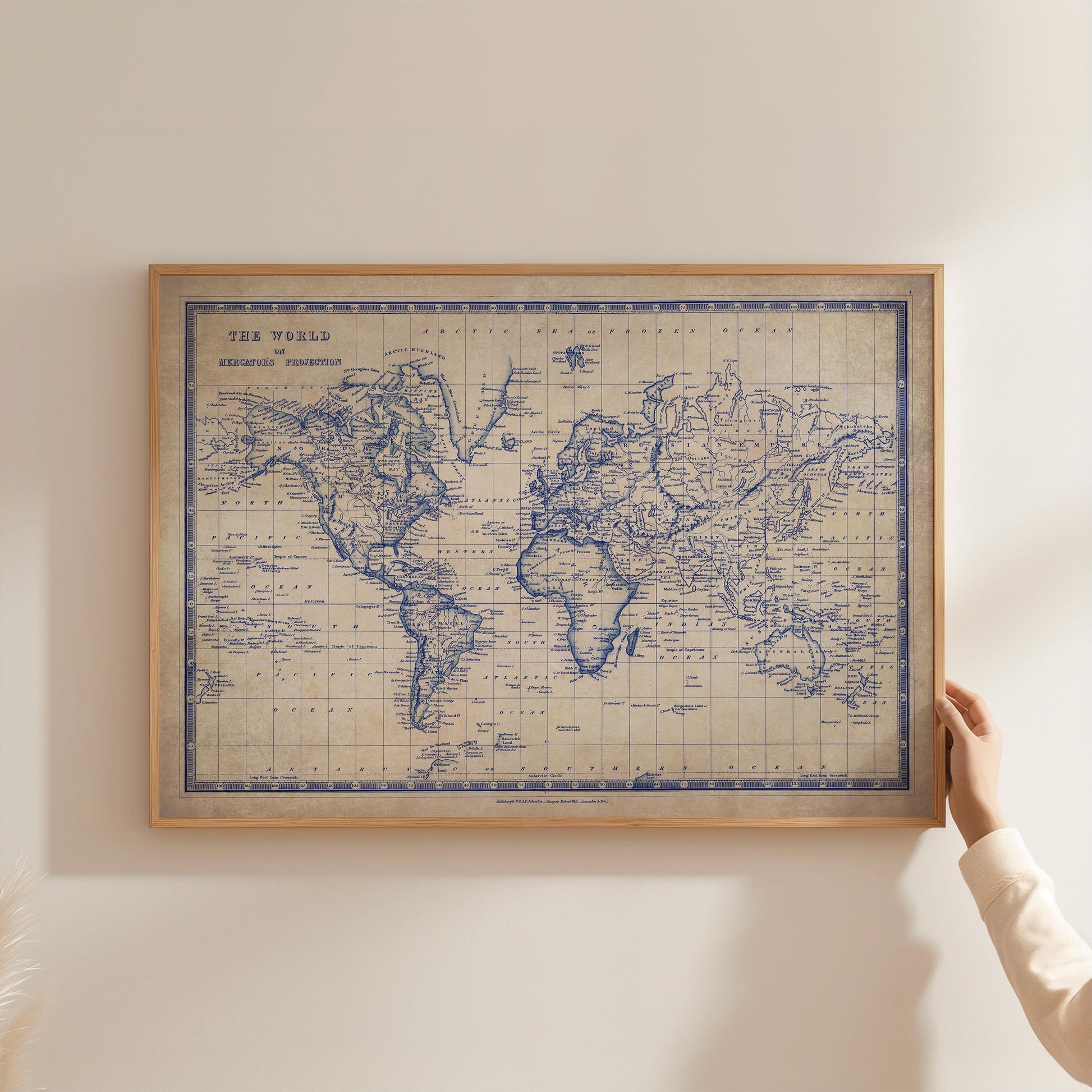 A person is holding up a framed world map, which appears to be an old map with blue coloring.