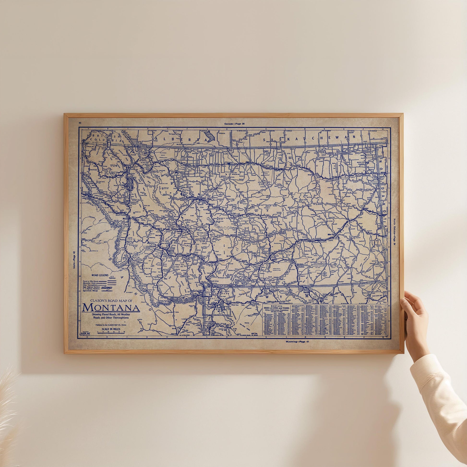 A framed map of Montana, showing the state's roads and highways, is being held up against a white wall.