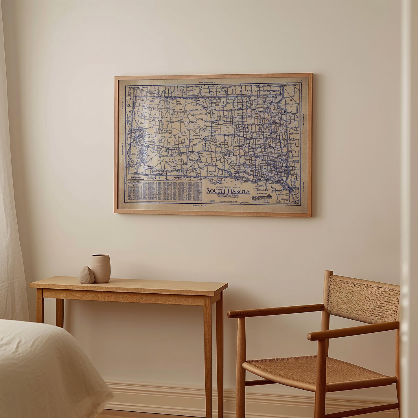 a wooden table with a small vase on it, and a chair is positioned next to the table. Above the table, there is a framed map of South Dakota hanging on the wall.