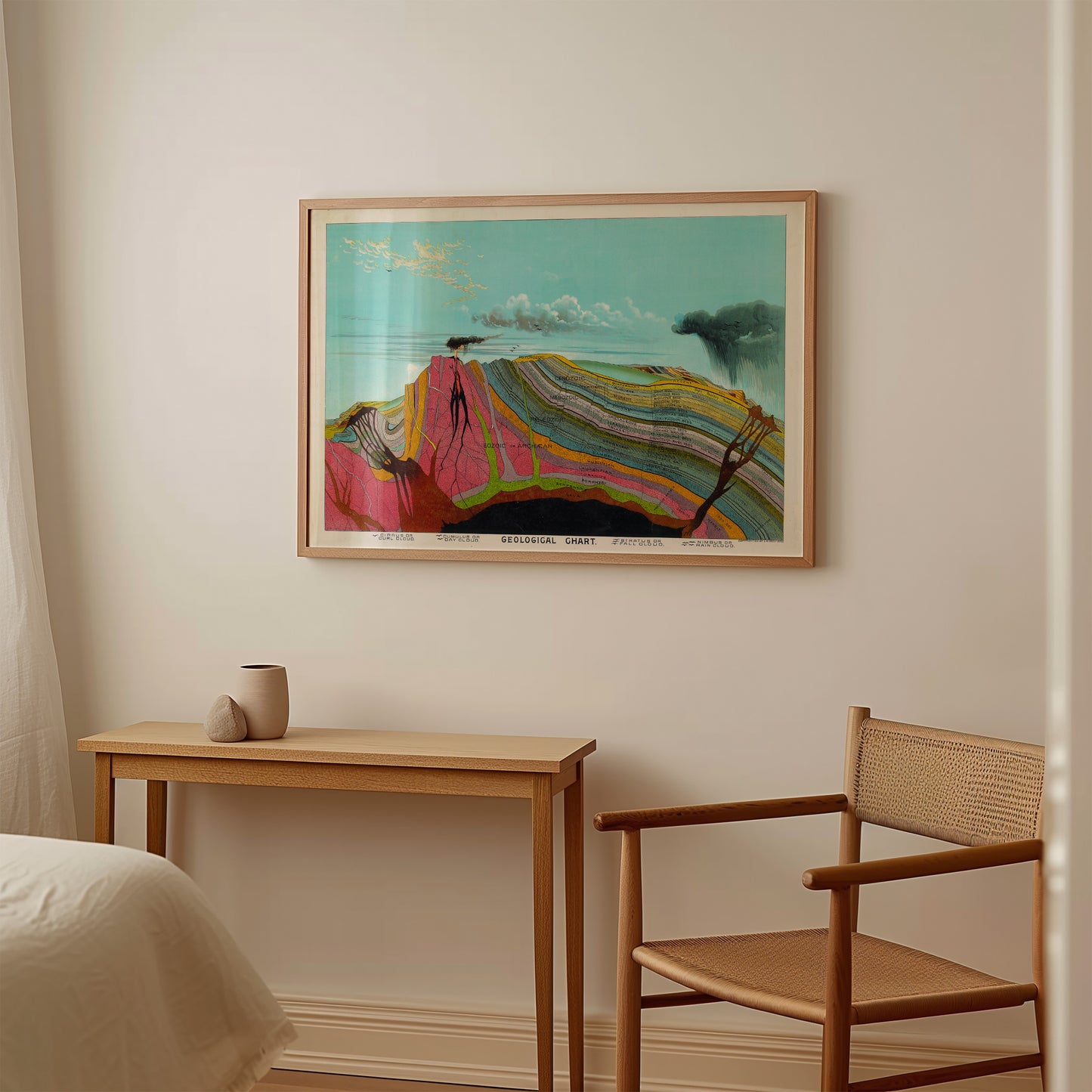 a wooden table with a small white mug on it, and a wooden chair next to it. Above the table, there is a framed painting hanging on the wall.