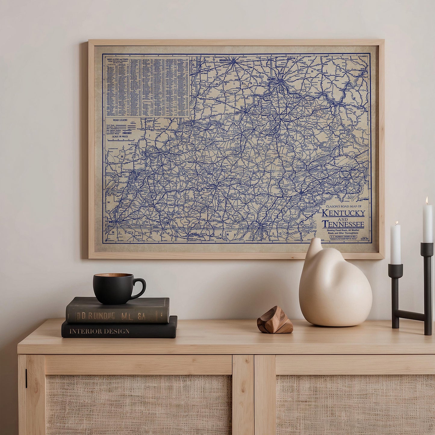 a framed map of Kentucky, a black coffee mug, a stack of books, a ceramic cat figurine, and a candle on a wooden shelf.