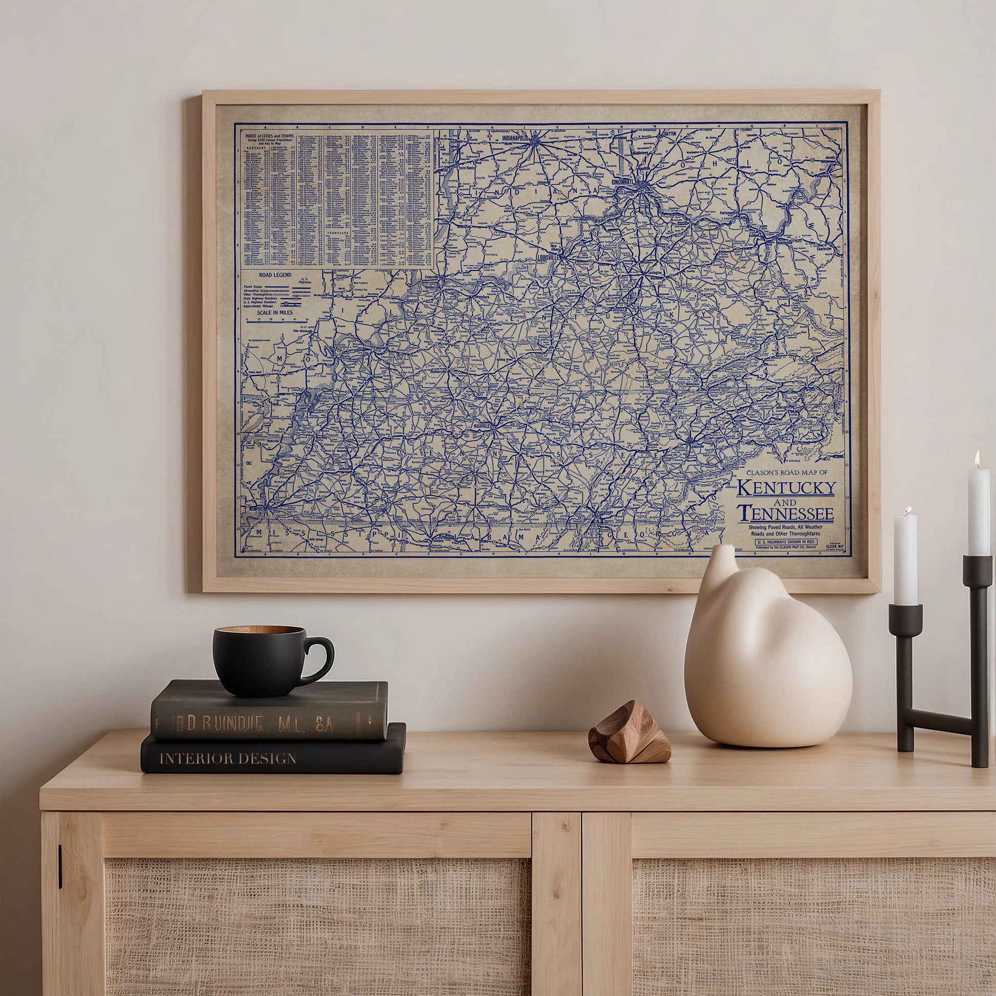 a framed map of Kentucky, a black coffee mug, a stack of books, a ceramic cat figurine, and a candle on a wooden shelf.