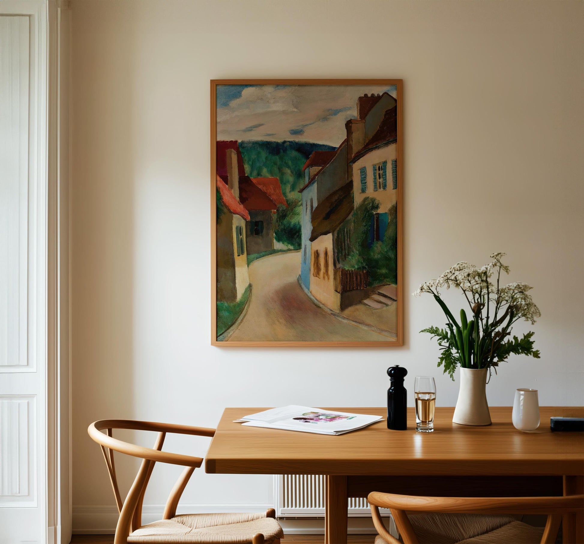 a cozy dining area with a wooden table, two chairs, and a framed painting of a picturesque village scene hanging on the wall above the table.