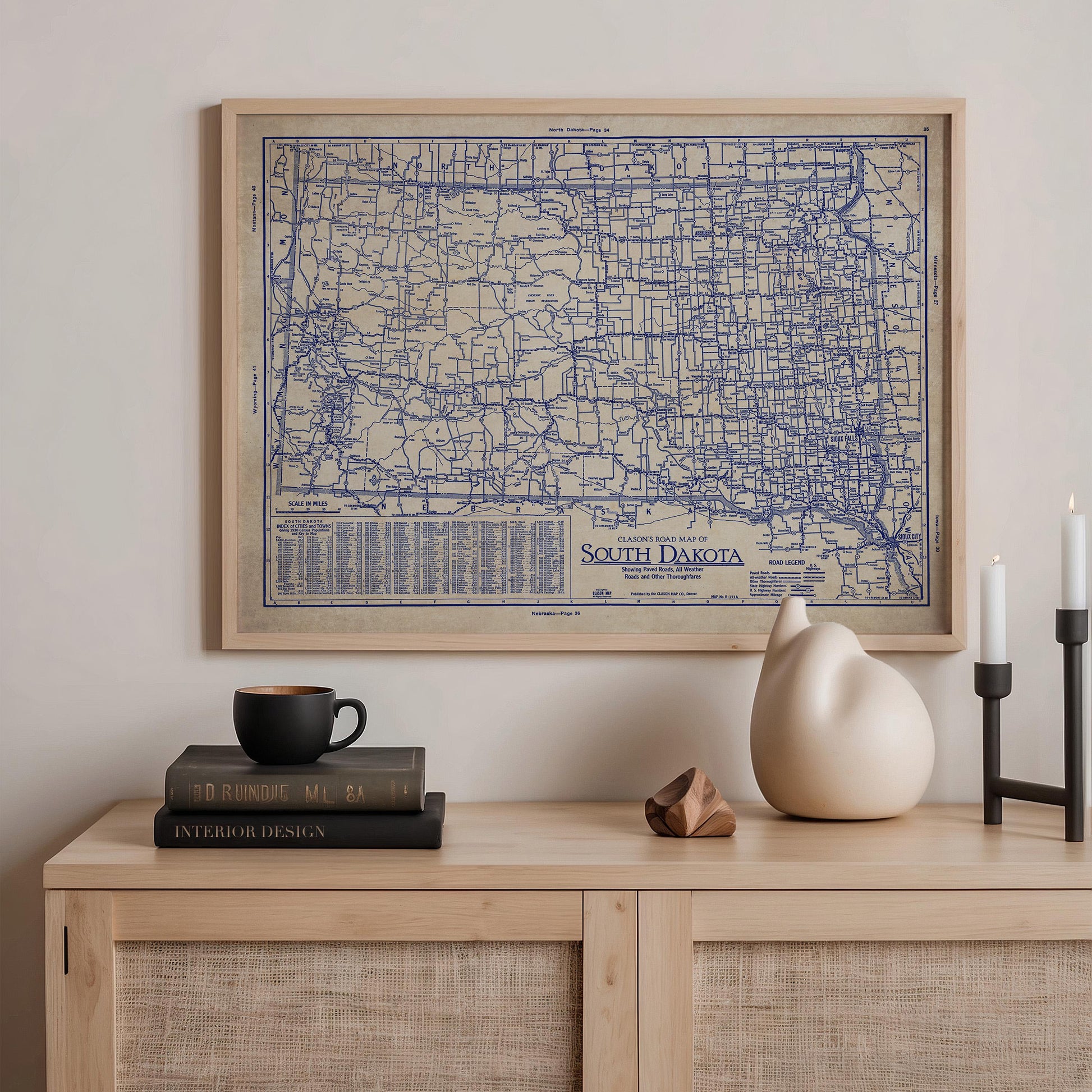 a wooden cabinet with a framed map of South Dakota hanging on the wall above it. On the cabinet, there are a stack of books, a ceramic cat figurine, and a small white vase.