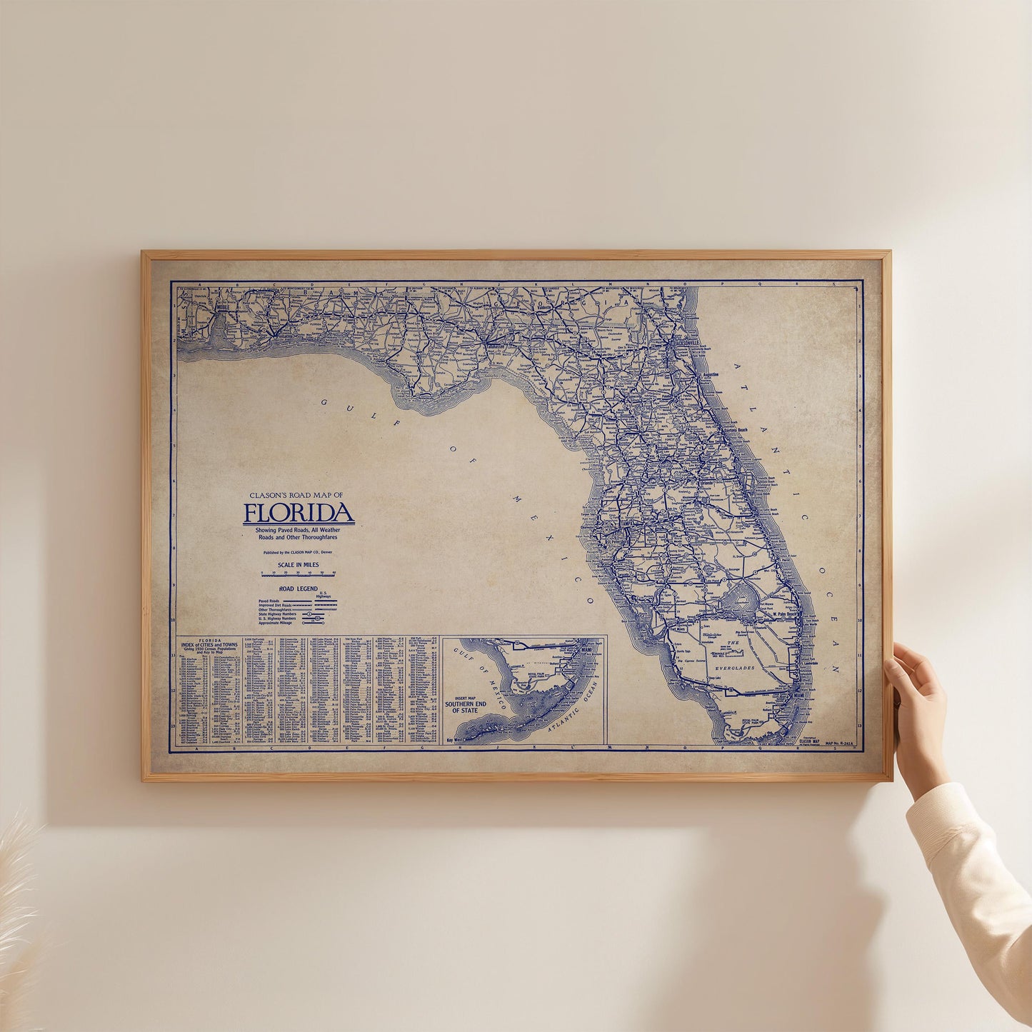 A framed map of Florida is being held up against a white wall.