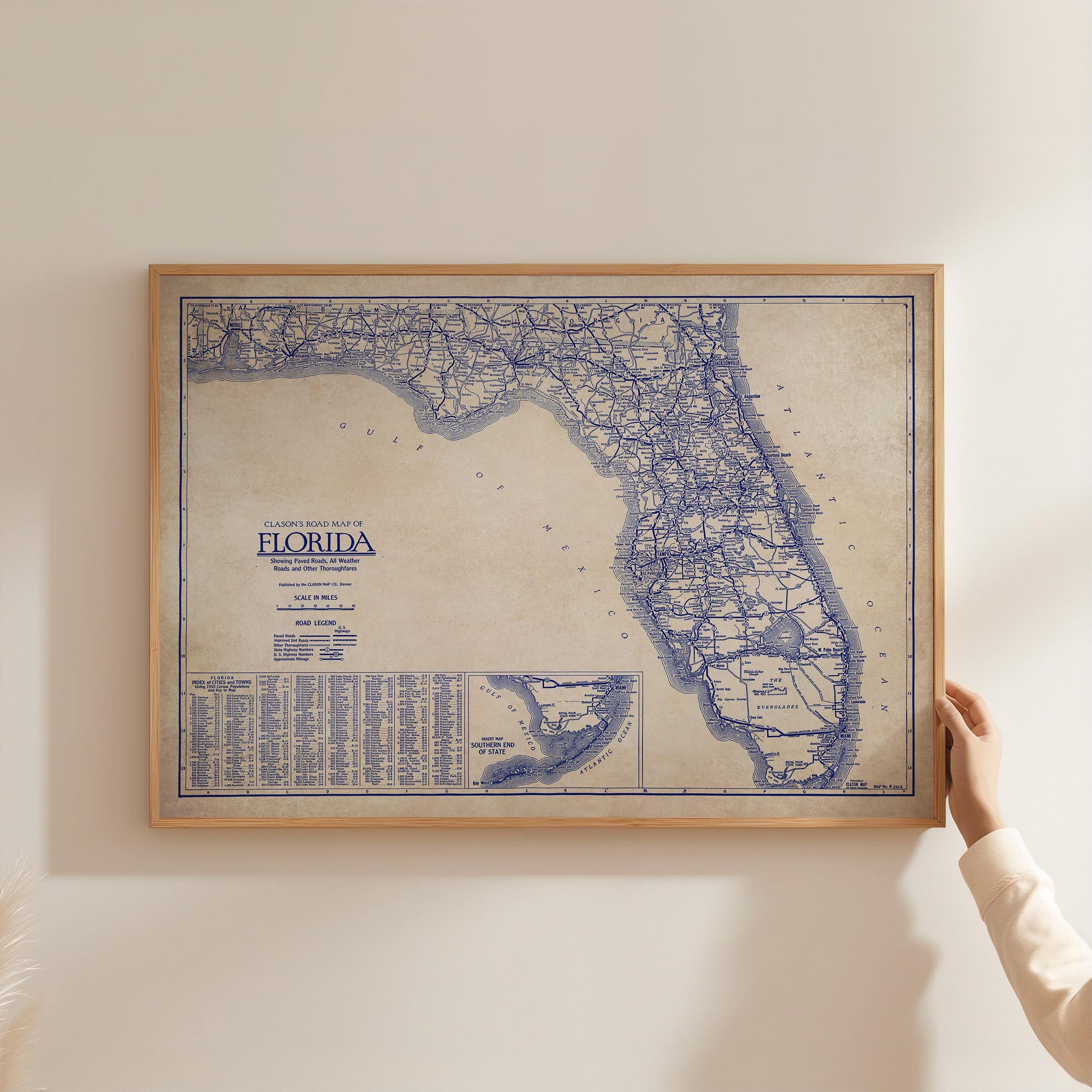 A framed map of Florida is being held up against a white wall.