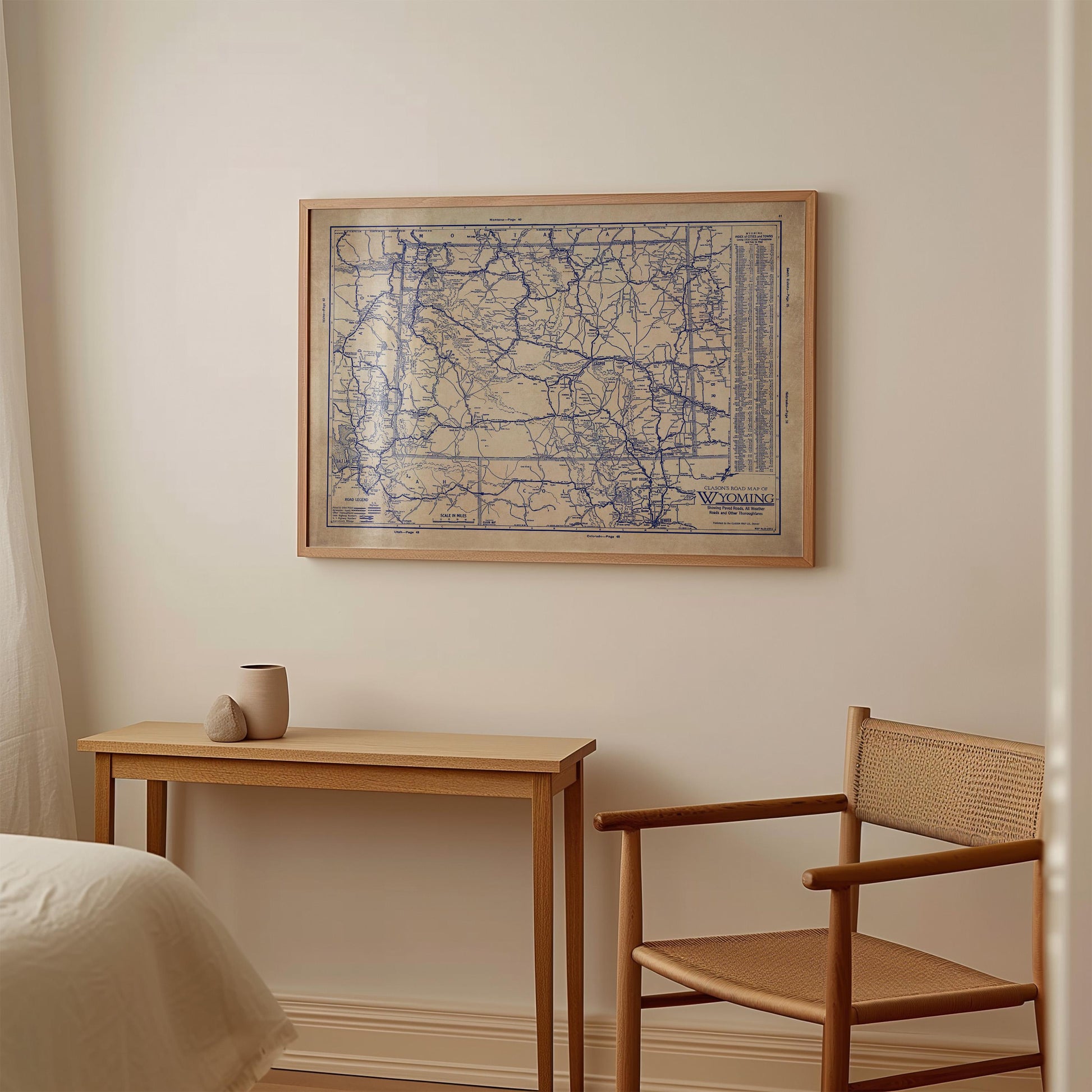 a wooden table with a small vase on it, and a wooden chair next to it. Above the table, there is a framed map hanging on the wall.