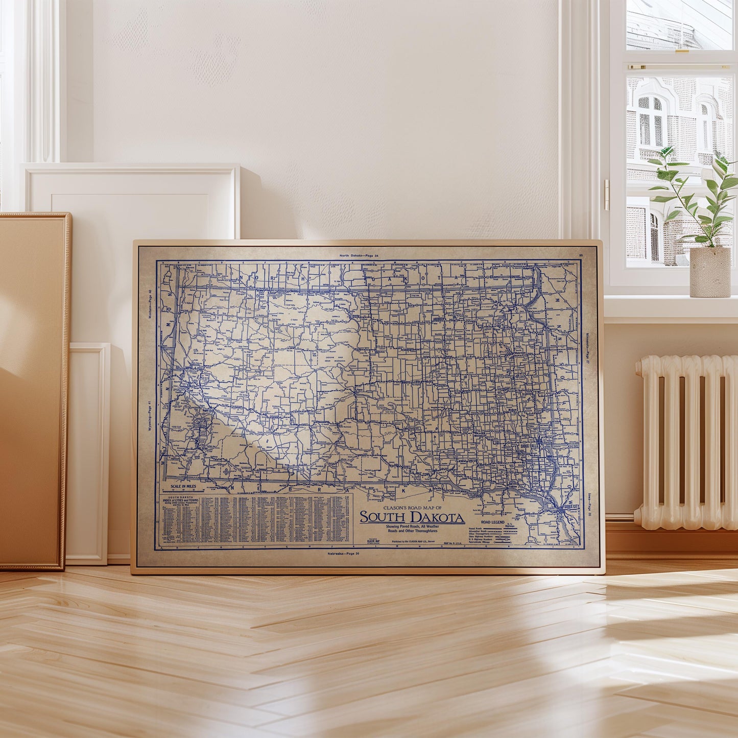 A framed map of South Dakota is displayed on a wooden floor in a room with a window and a radiator.