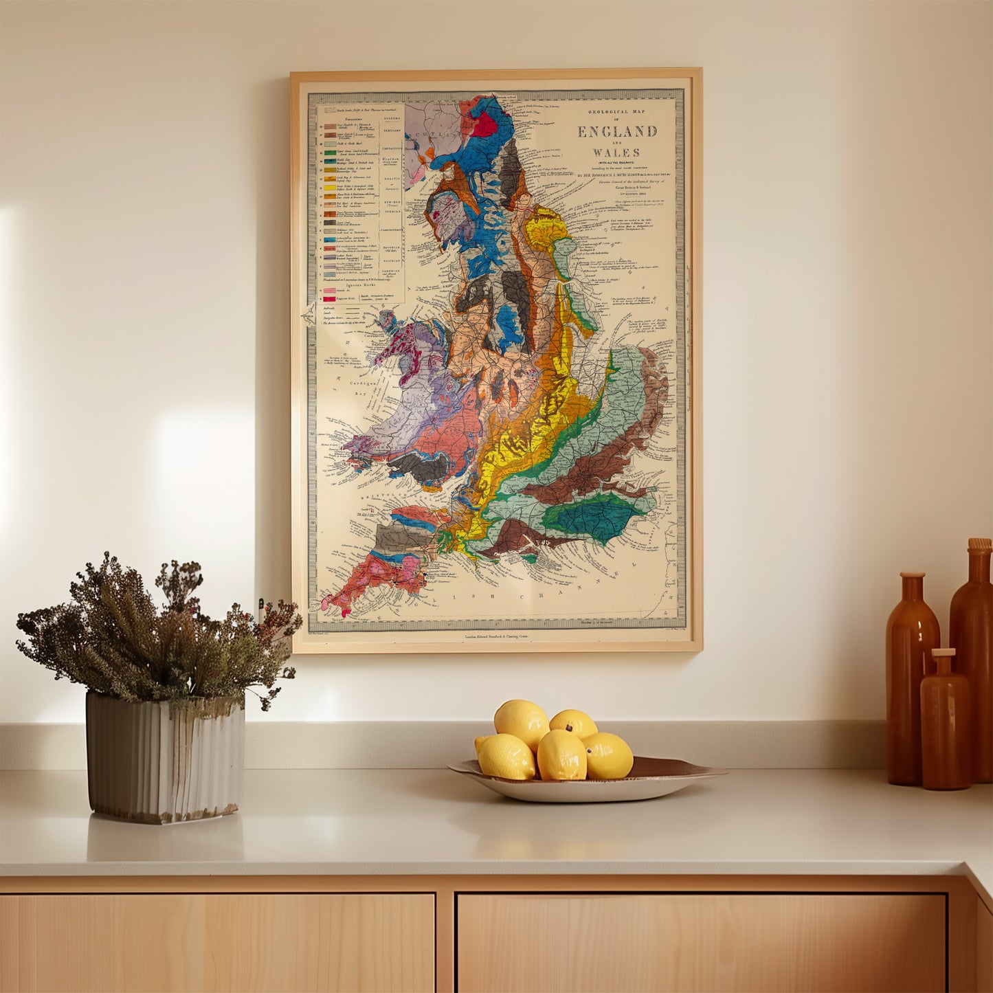 a kitchen counter with a framed map of England and Wales hanging above it, a bowl of fruit, and some decorative items on the counter.