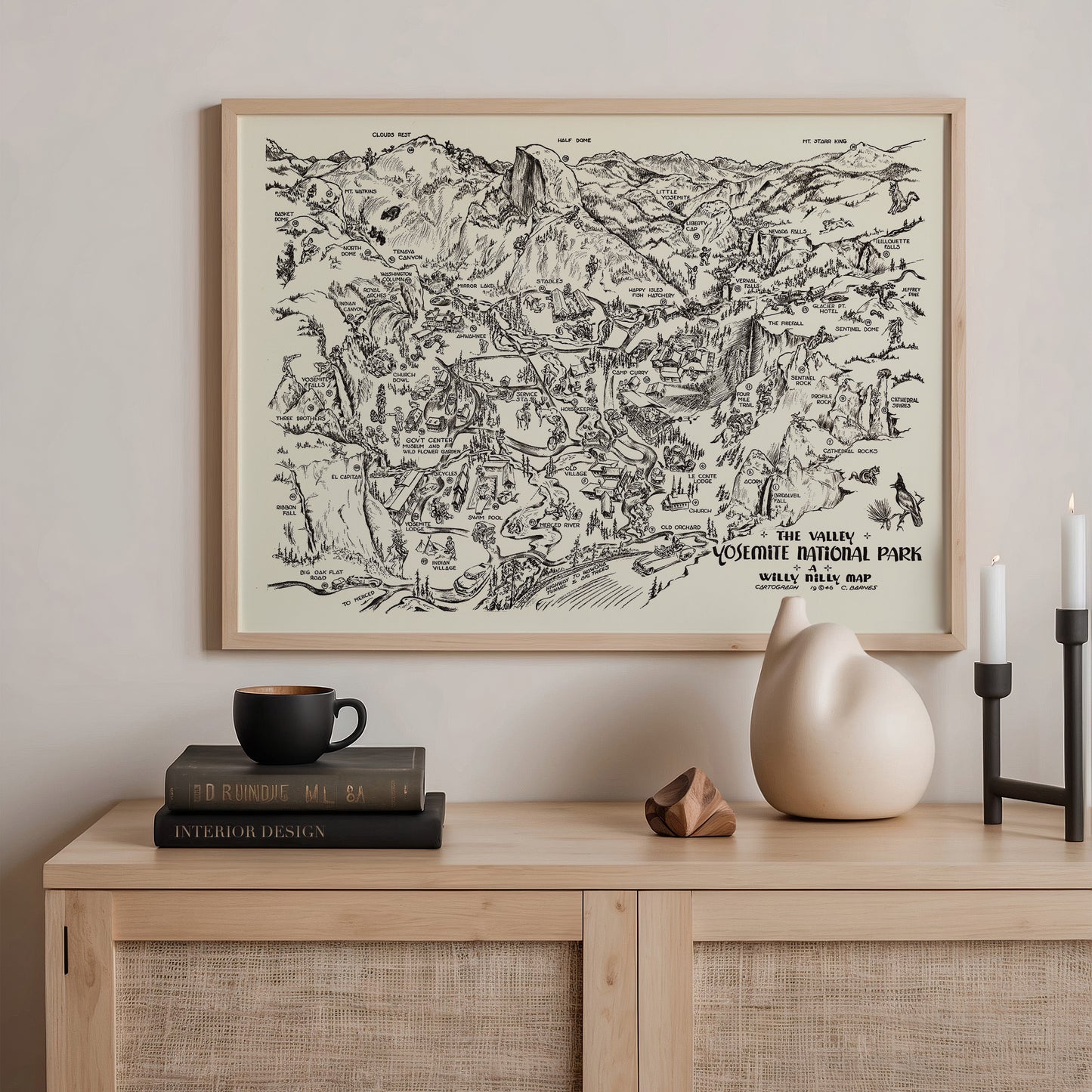 a framed map of Yosemite National Park, with a black and white illustration of the park's landscape and various landmarks. The map is hanging on a wall above a wooden dresser, which has a stack of books, a ceramic vase, and a candle on it.