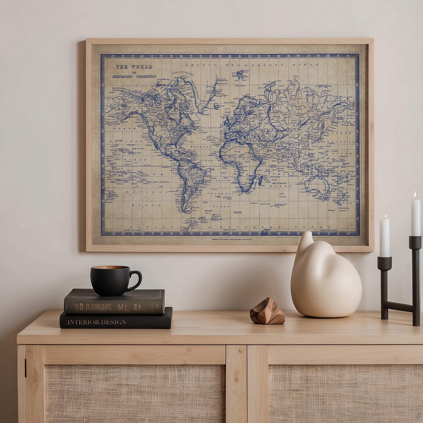 a framed vintage world map hanging on a wall above a wooden dresser. On the dresser, there are a stack of books, a ceramic vase, and a small sculpture.