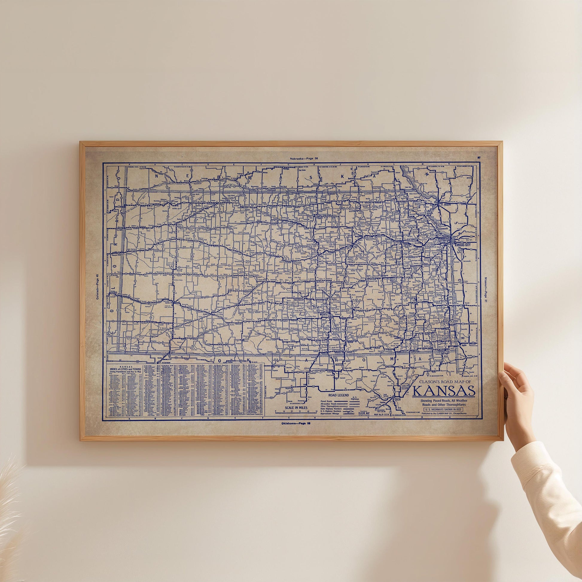 A framed map of Kansas is being held up against a white wall.