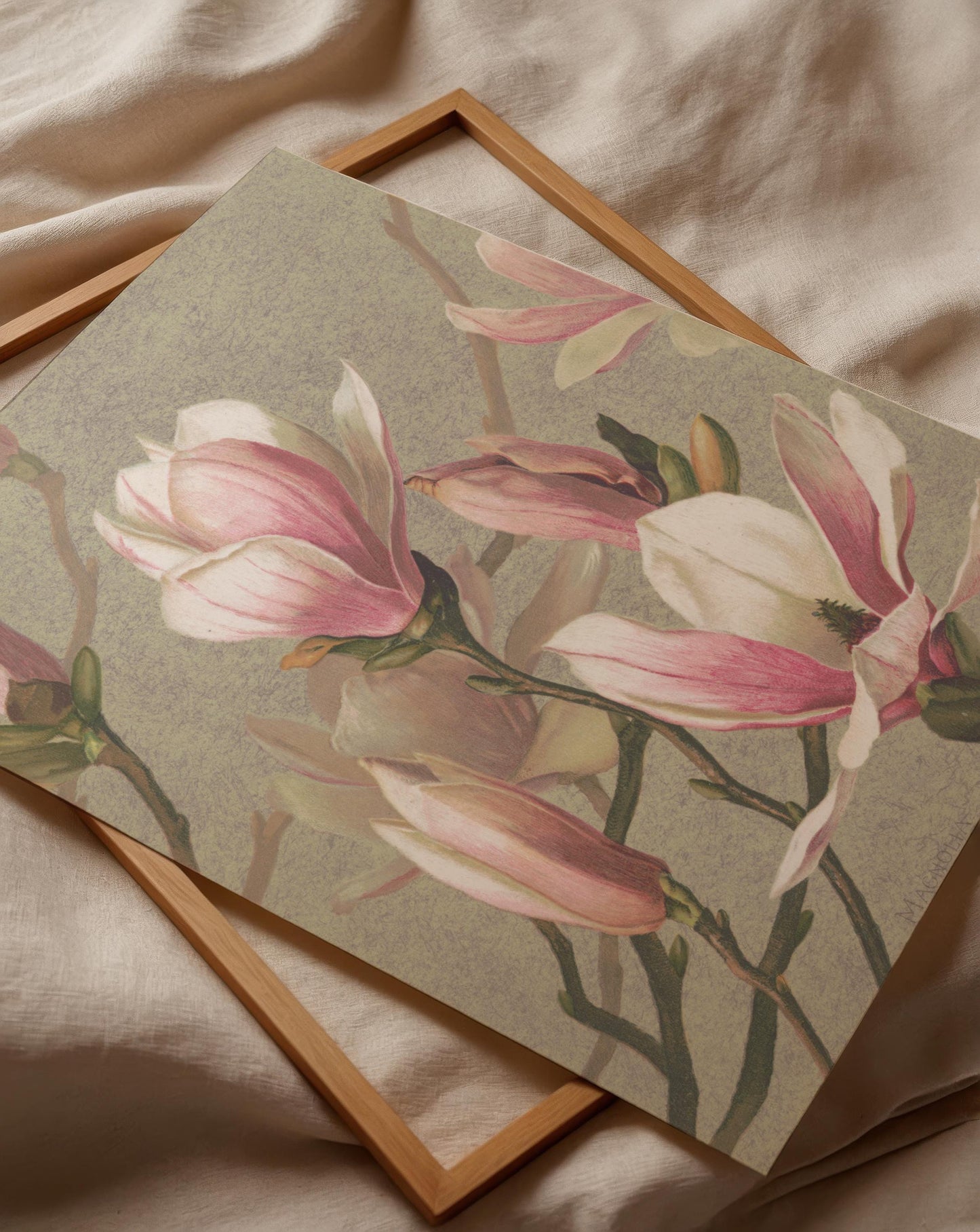 a framed print of a floral design with pink and white flowers, placed on a beige fabric surface.