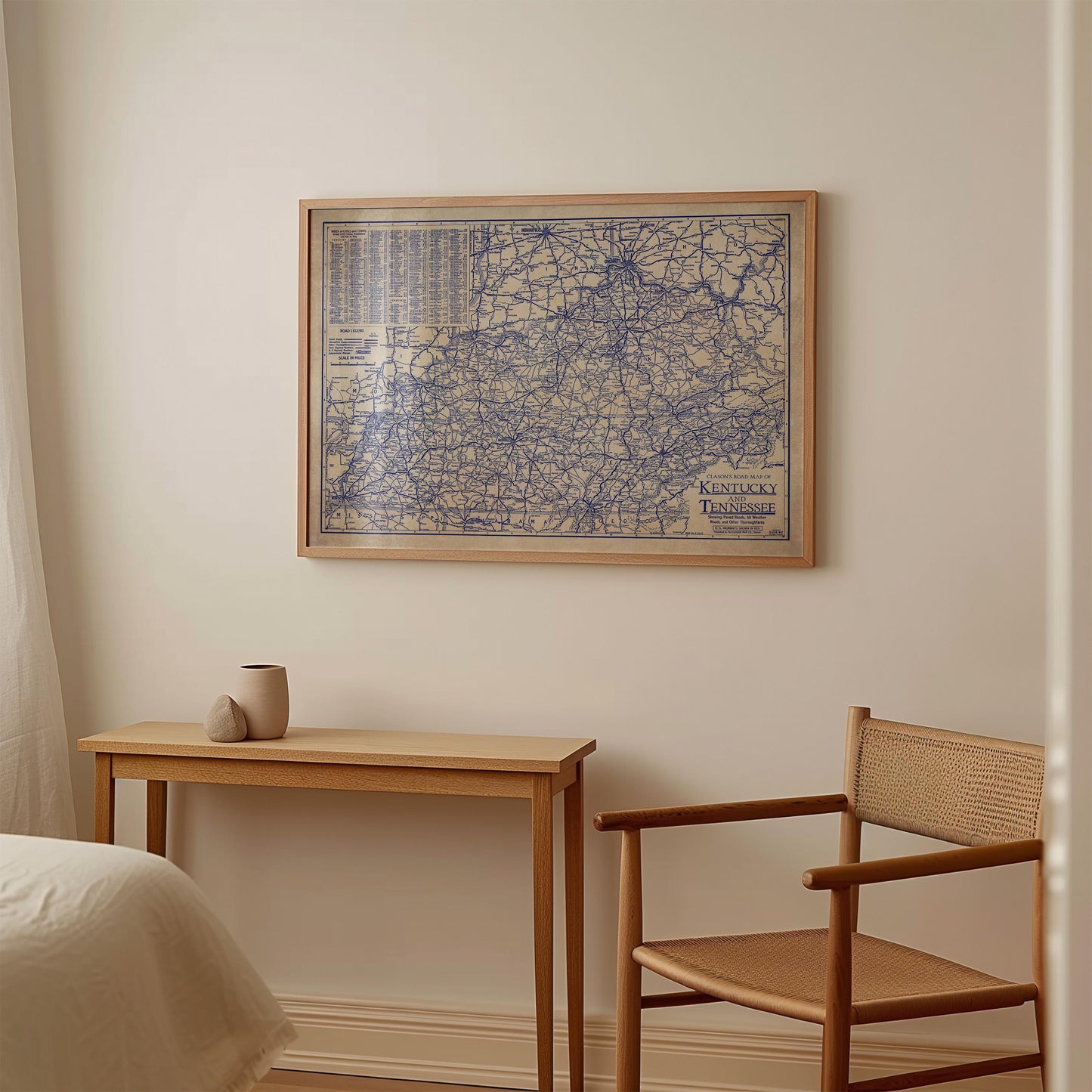 a wooden table with a small vase on top, and a wooden chair next to it. Above the table, there is a framed map hanging on the wall.