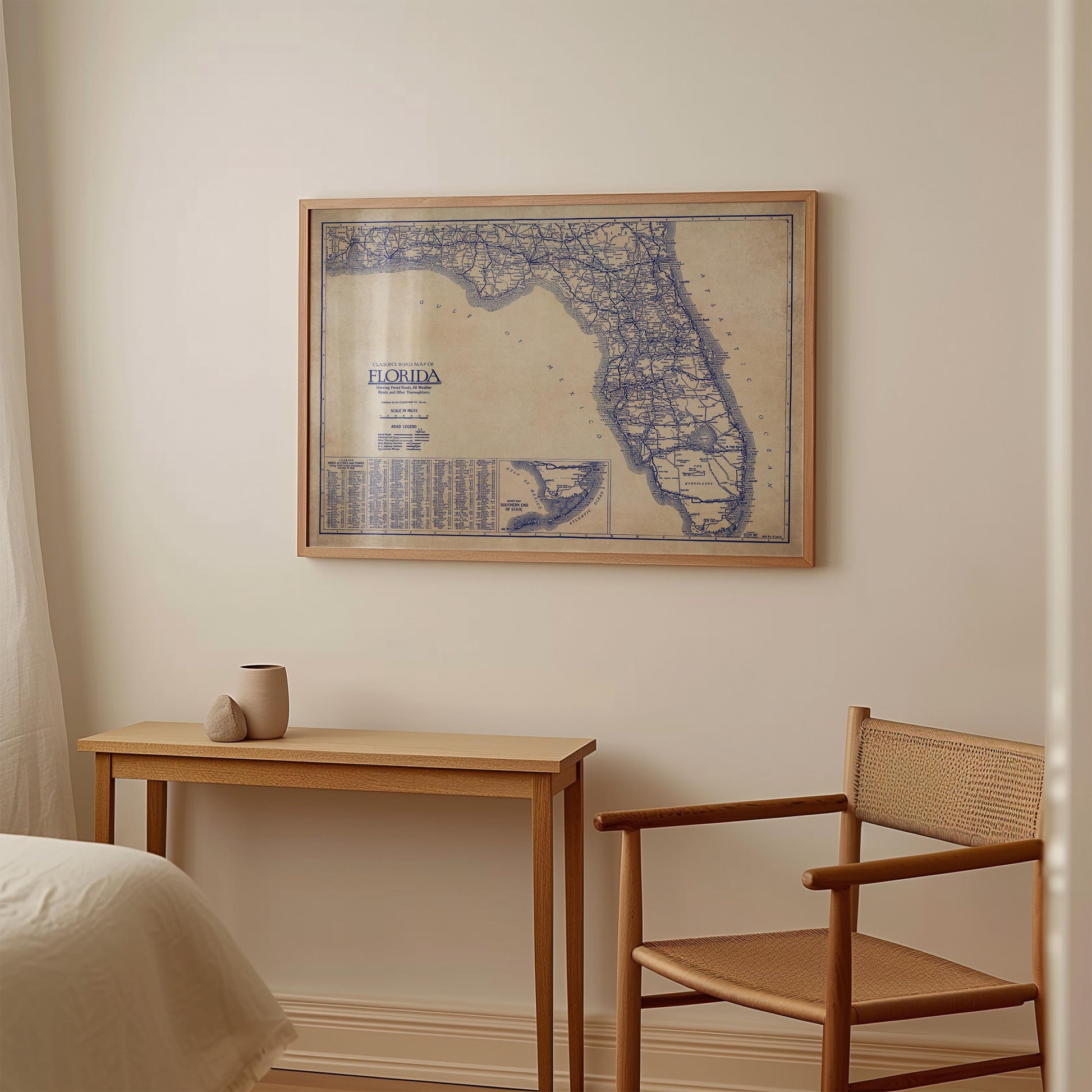 a framed map of Florida hanging on a wall, with a small table and a chair positioned below it.