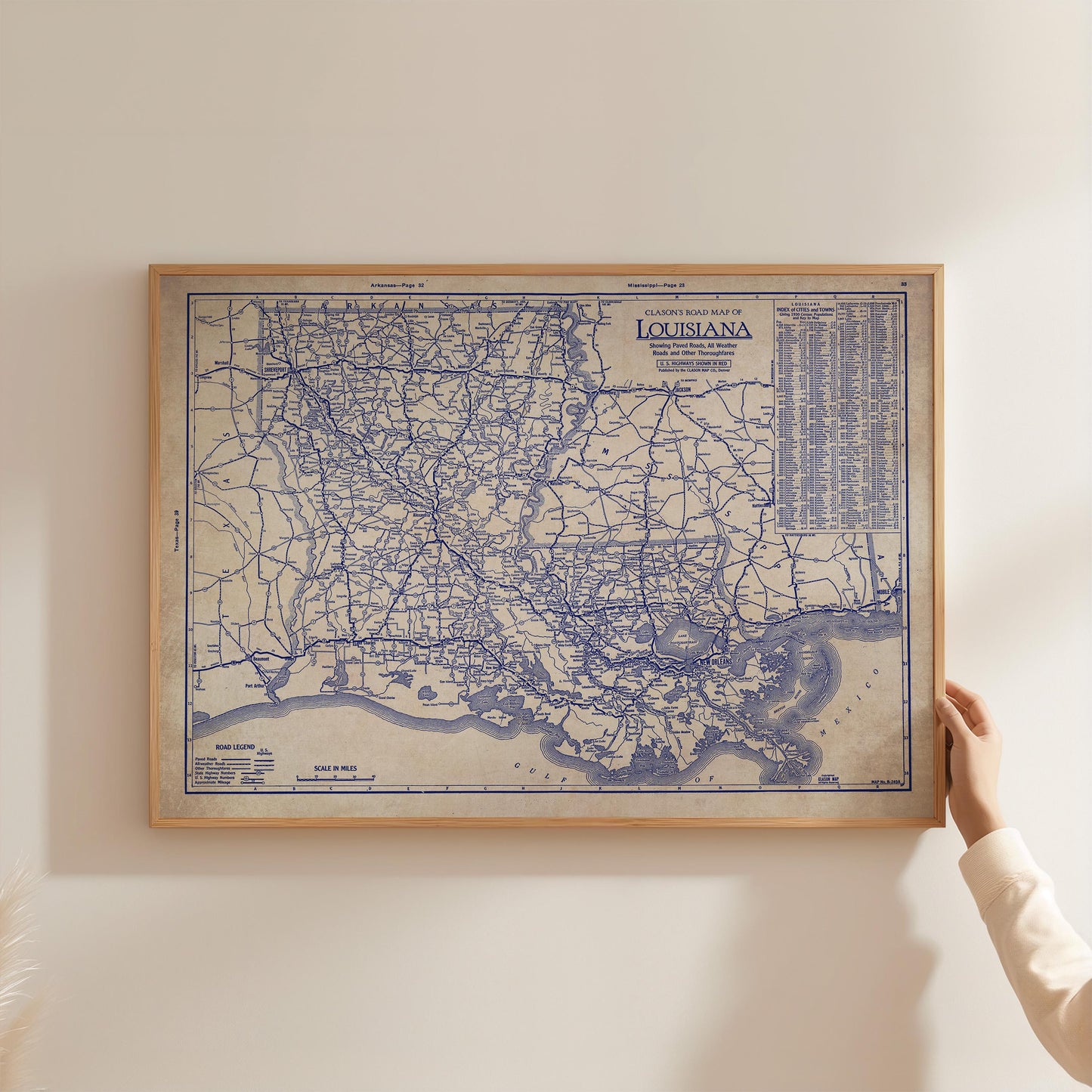 A framed map of Louisiana, showing the state's road network, is being held up against a white wall.