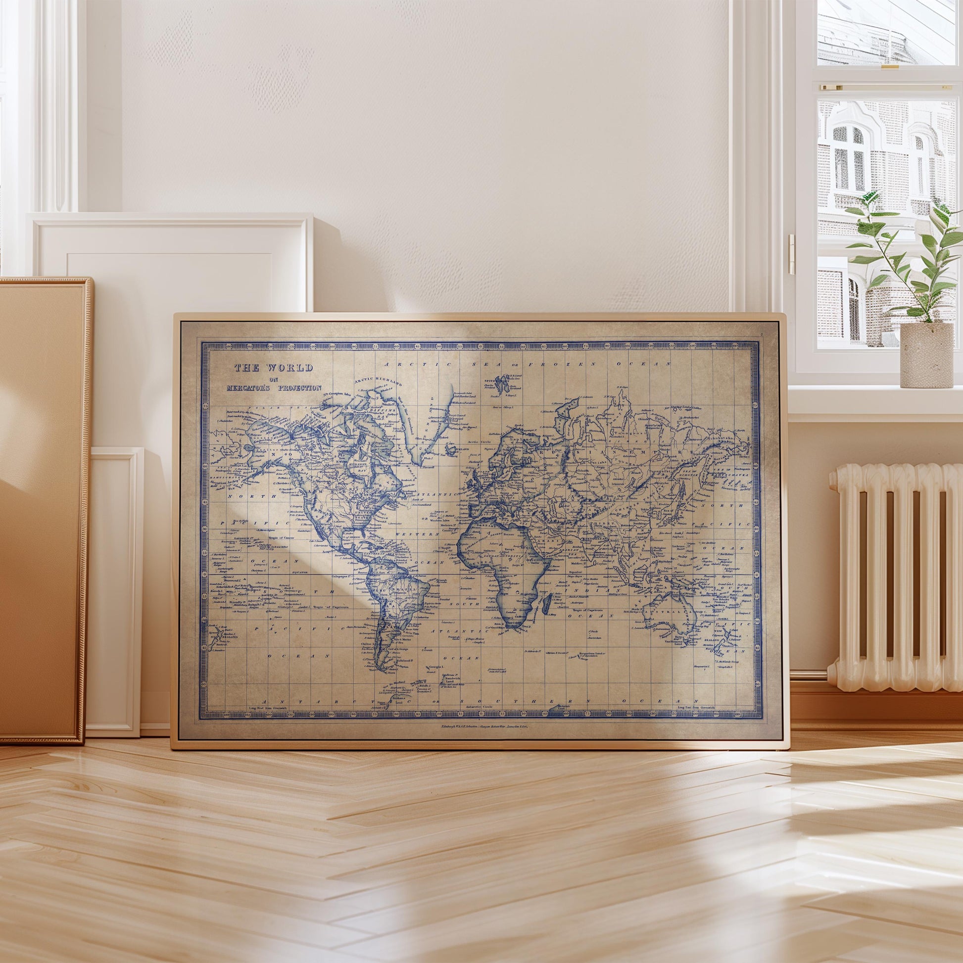 A framed vintage world map is displayed on a wooden floor in a room with a window and a radiator.