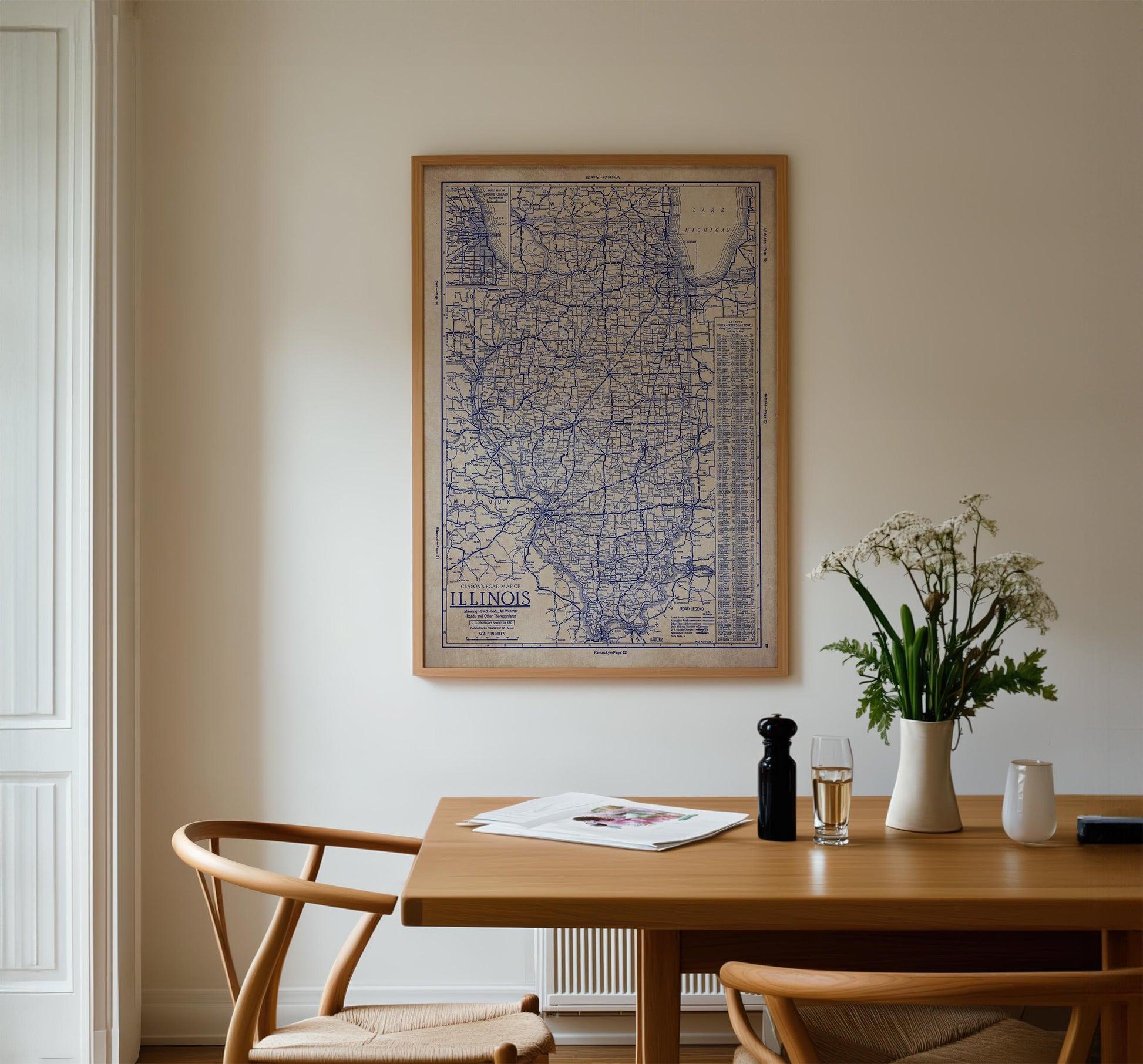 a dining room with a wooden table, two chairs, a framed map of Illinois hanging on the wall, and a vase of flowers on the table.