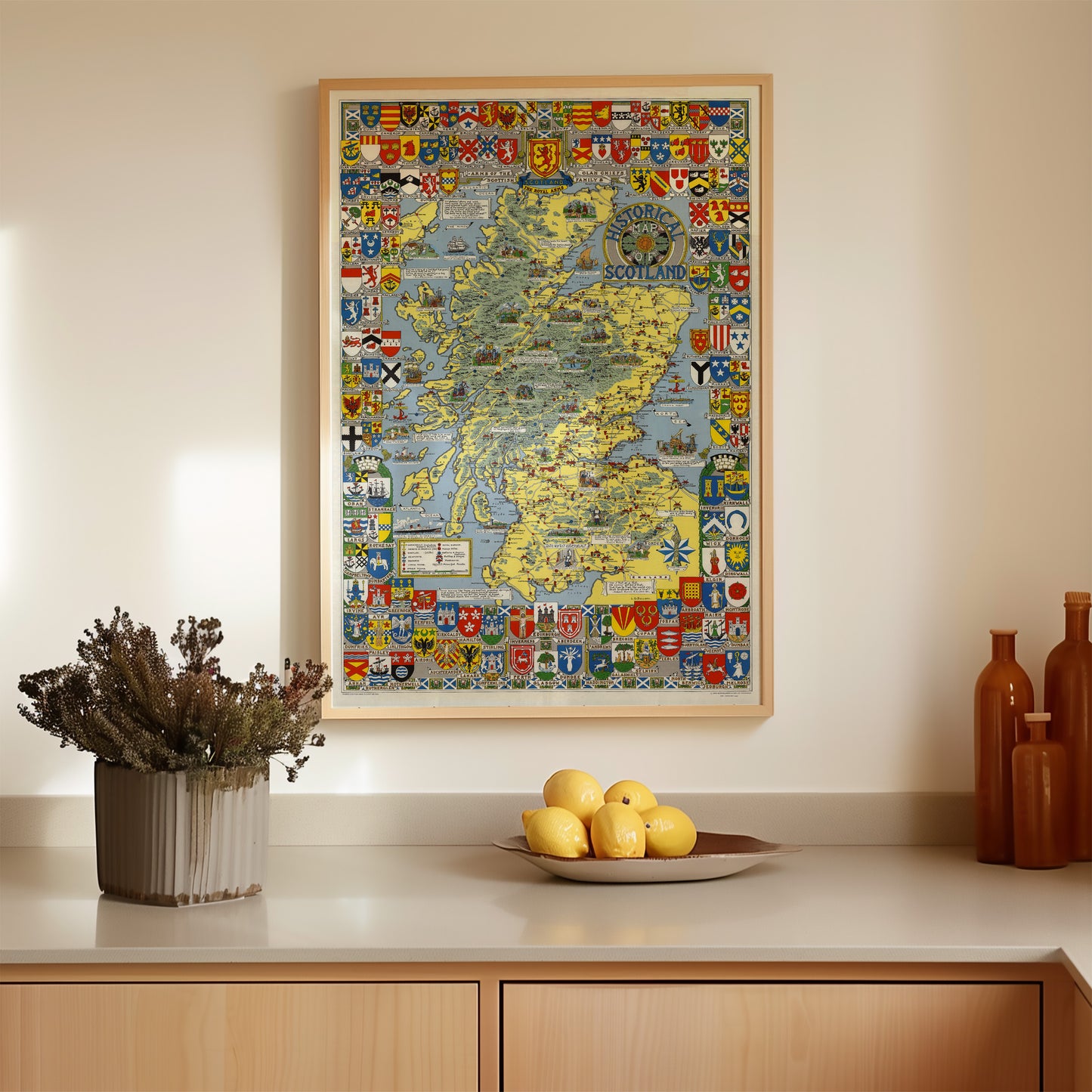 a kitchen counter with a framed map of Scotland hanging above it, a bowl of lemons, and a vase of dried flowers.
