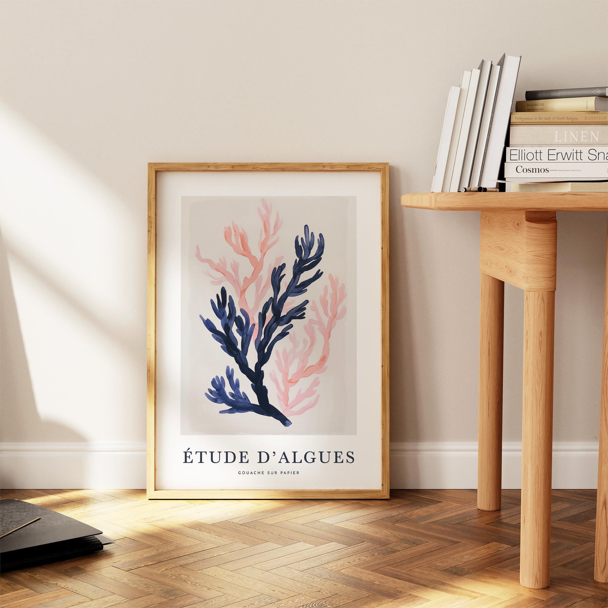 a framed artwork titled "Étude d'Algues" by Gómez-Llinas, displayed on a wooden floor next to a wooden table with books.