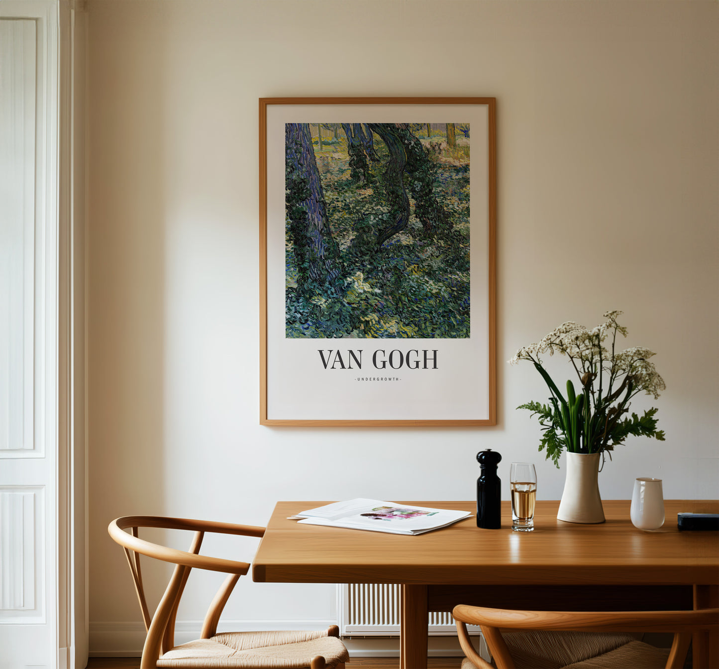 a dining table with a vase of flowers, a newspaper, and a bottle of wine. Above the table, there is a framed painting of a forest scene.