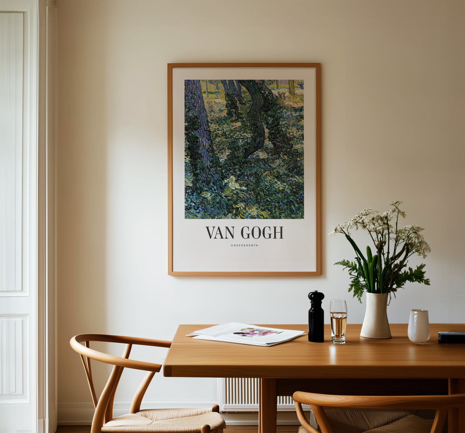 a dining table with a vase of flowers, a newspaper, and a bottle of wine. Above the table, there is a framed painting of a forest scene.