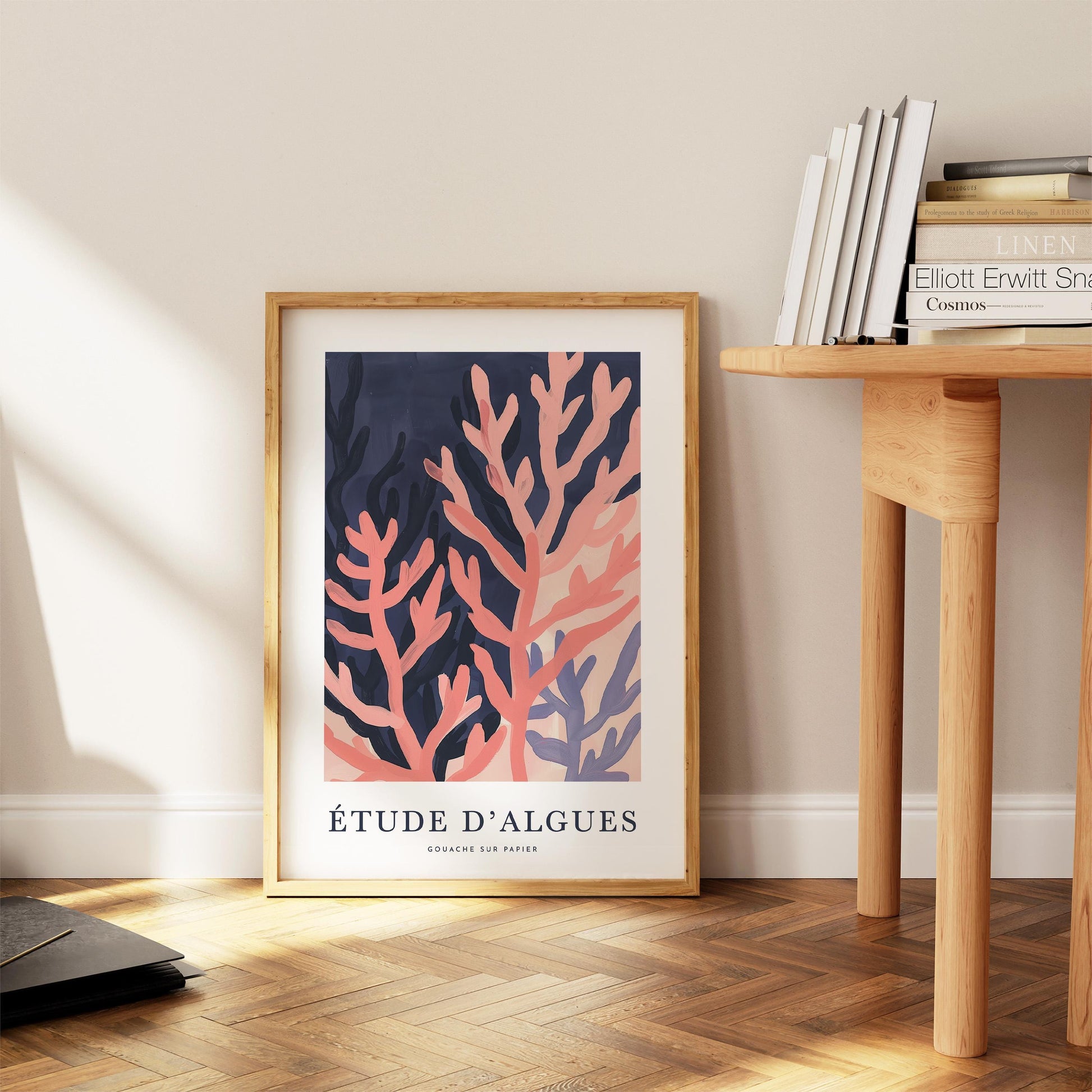 a framed poster of a coral reef with the text "Étude d'Algues" and "Gouche sur tous" on it, placed on a wooden floor next to a wooden table with books on it.