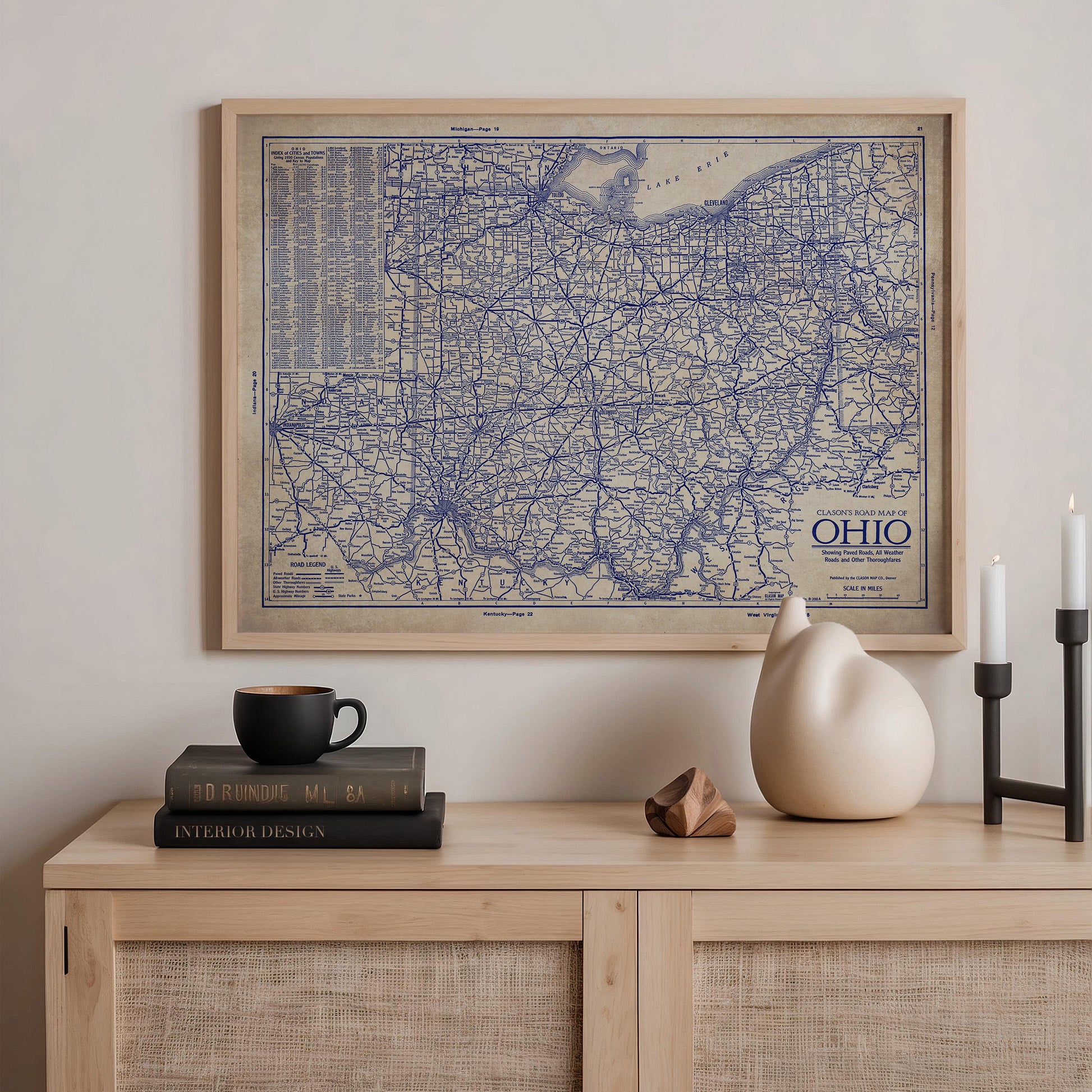 a framed map of the Ohio region hanging on a wall above a wooden shelf with various items on it, including a stack of books, a ceramic cat figurine, and a small white vase.