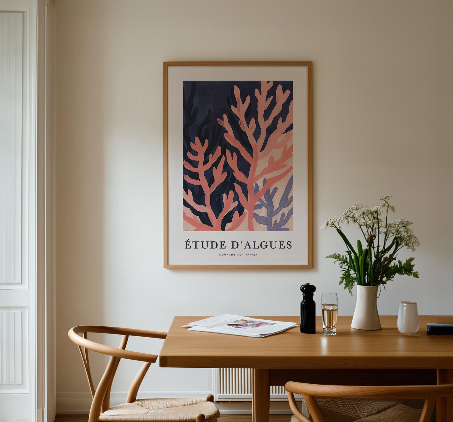 a dining room with a wooden table, two chairs, a framed poster of a coral design, and a vase of flowers.