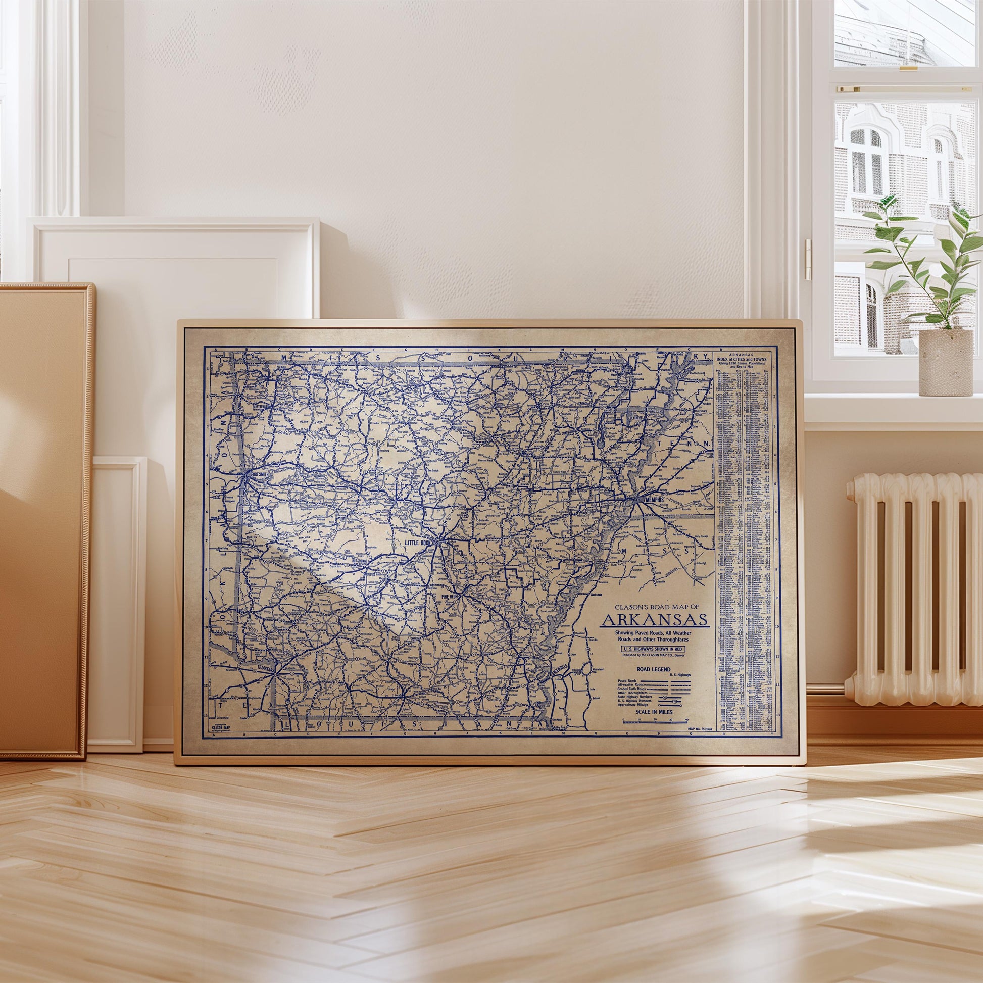 A framed map of the Arkansas region is displayed on a wooden floor in a room with a window and a radiator.