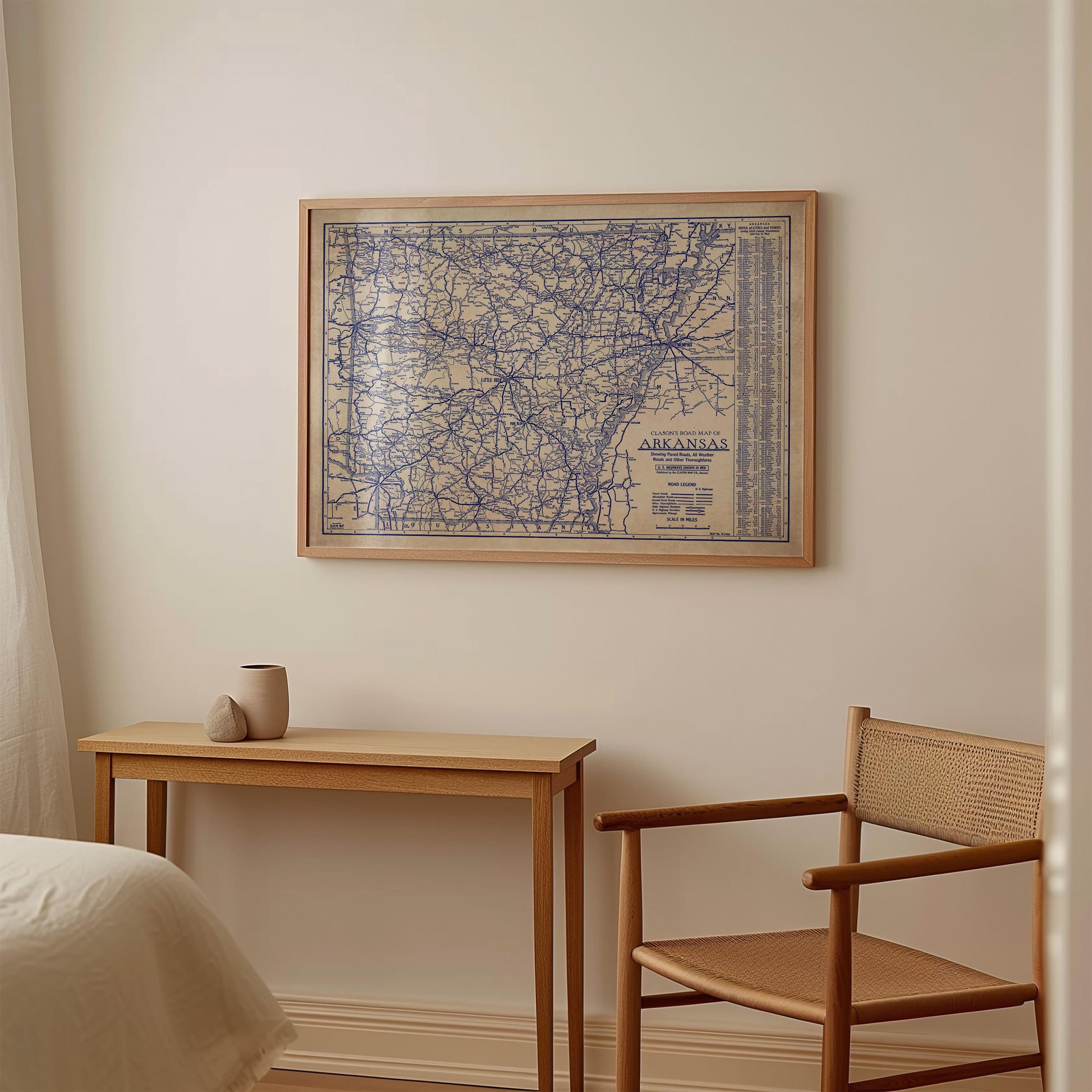 a wooden table with a small vase on it, and a wooden chair next to it. Above the table, there is a framed map of Alabama hanging on the wall.