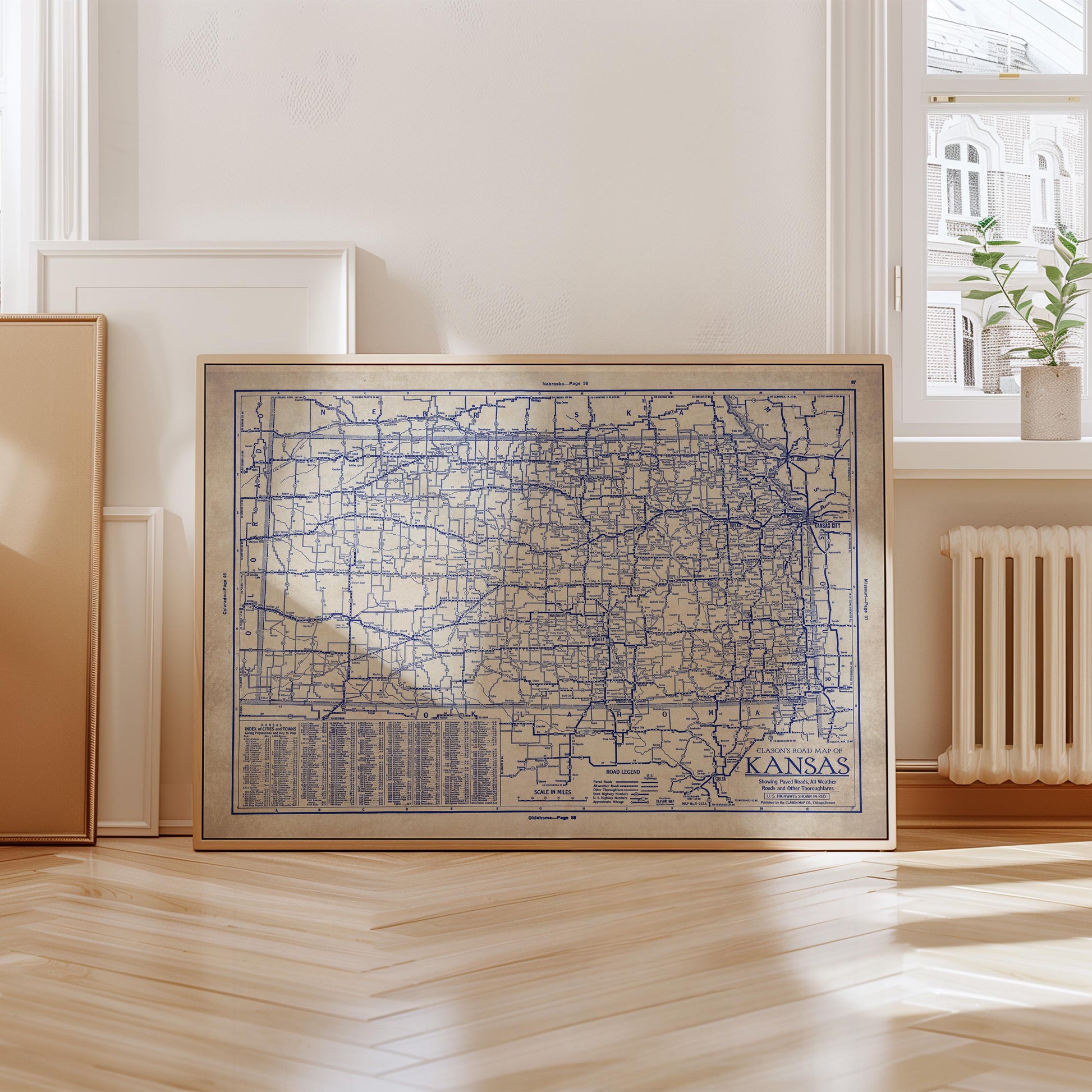 A framed map of Kansas is displayed on a wooden floor in a room with a window and a radiator.