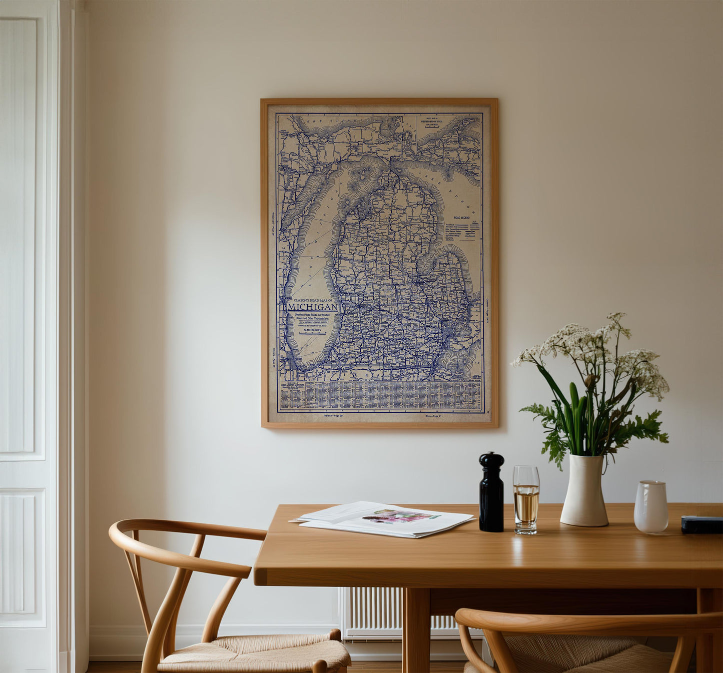a dining room with a wooden table, two chairs, a framed map of Michigan hanging on the wall, and a vase of white flowers on the table.