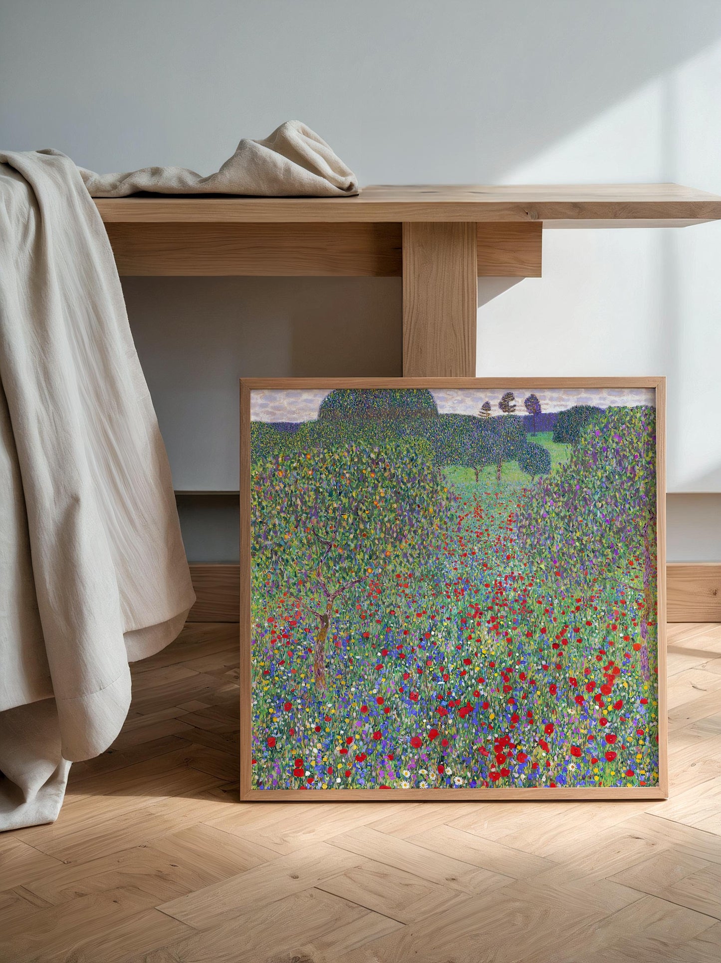 a framed painting of a field of flowers, with a wooden table and a beige cloth in the background.
