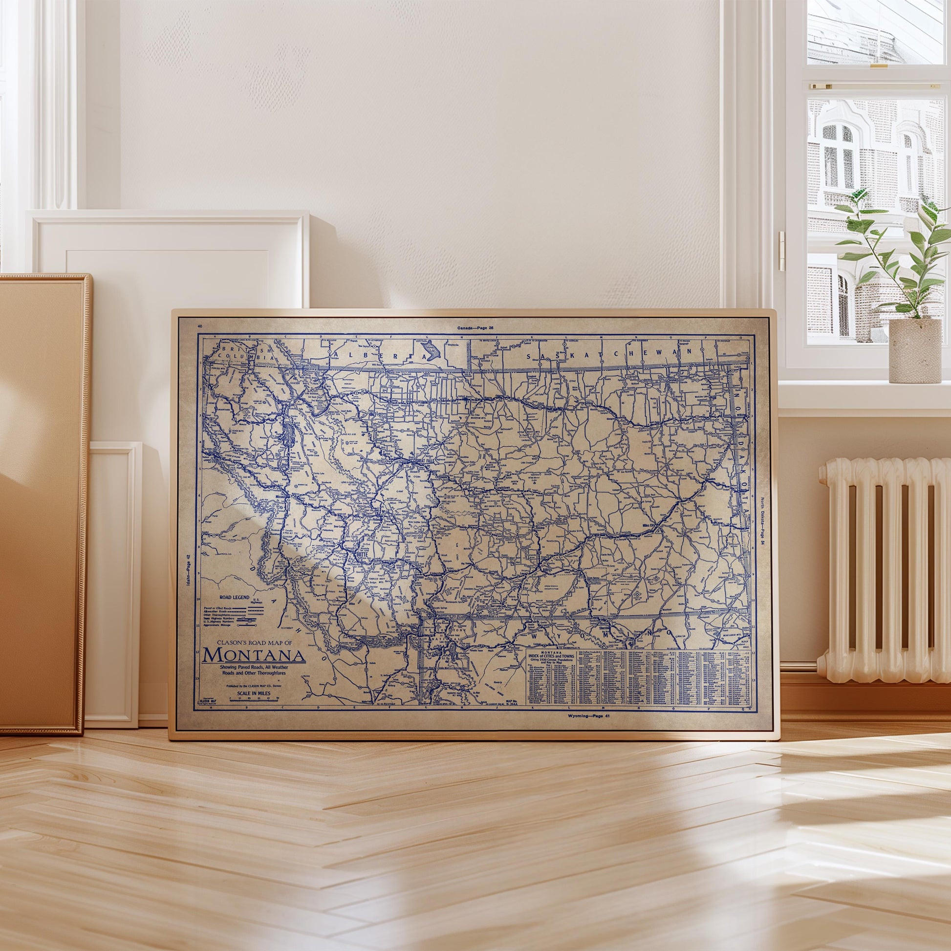 A framed map of Montana is displayed on a wooden floor in a room with a window and a radiator.