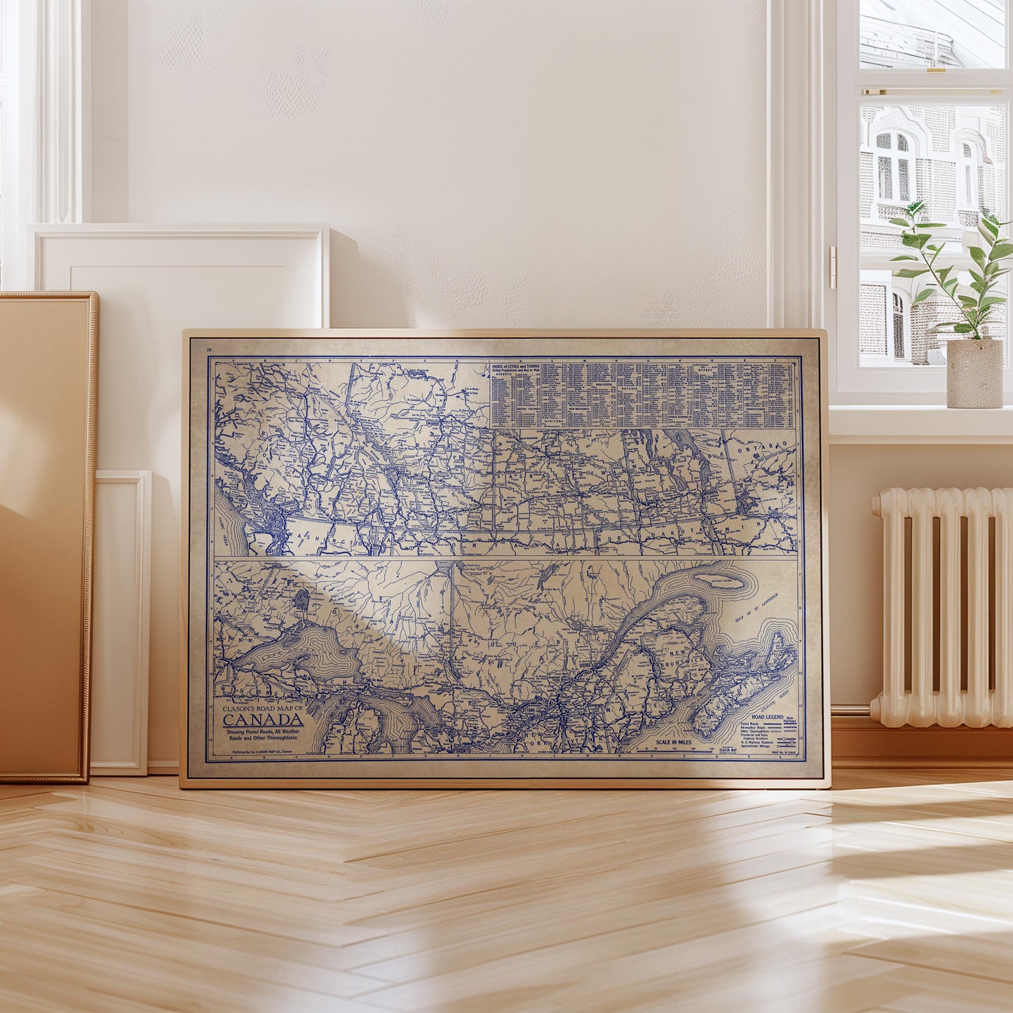 A framed map of Canada is displayed on a wooden floor in a room with a window and a radiator.